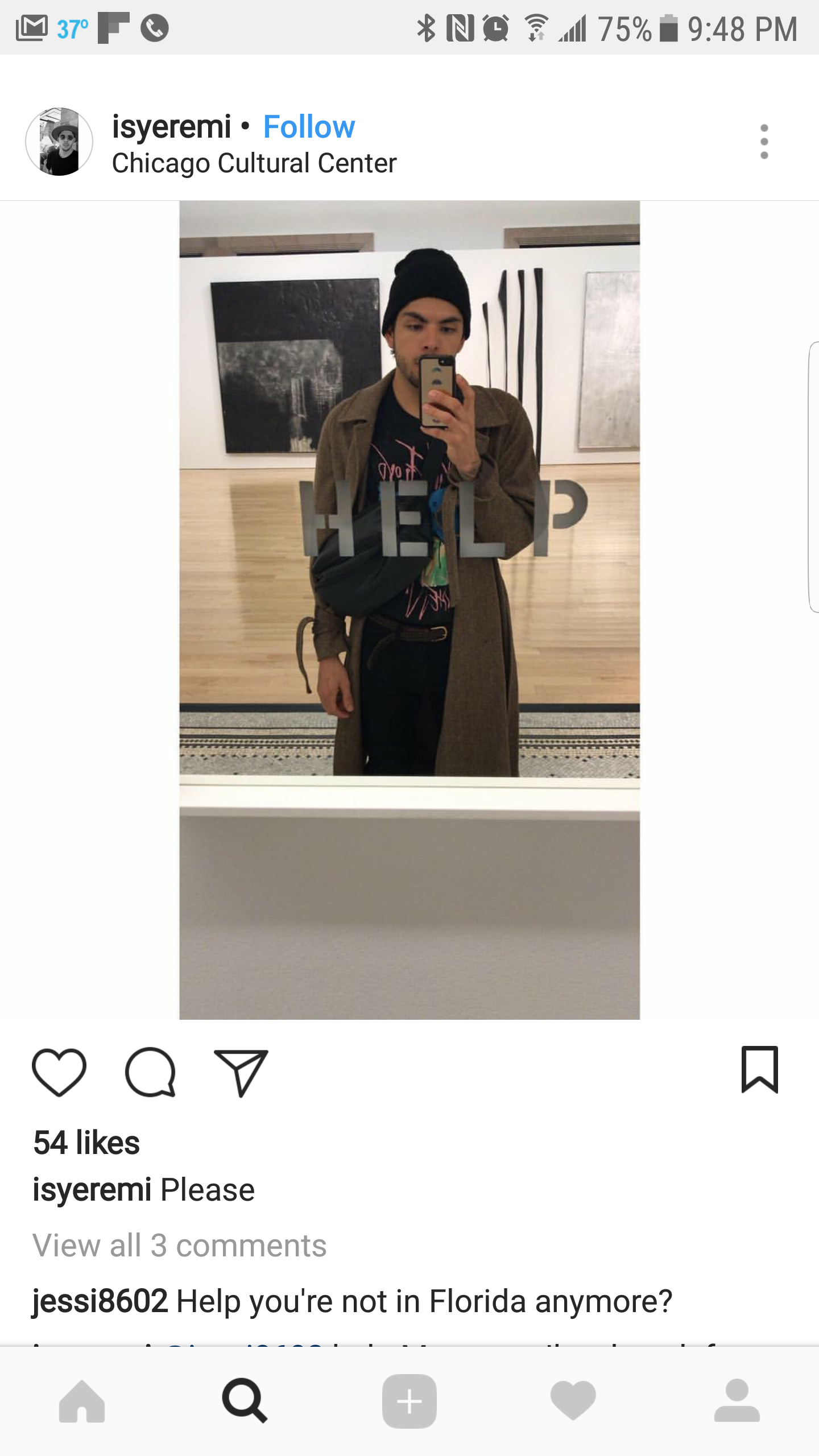 A young man taking a mirror selfie at the Chicago Cultural Center, wearing a black beanie, brown coat, and black T-shirt, with a black shoulder bag.