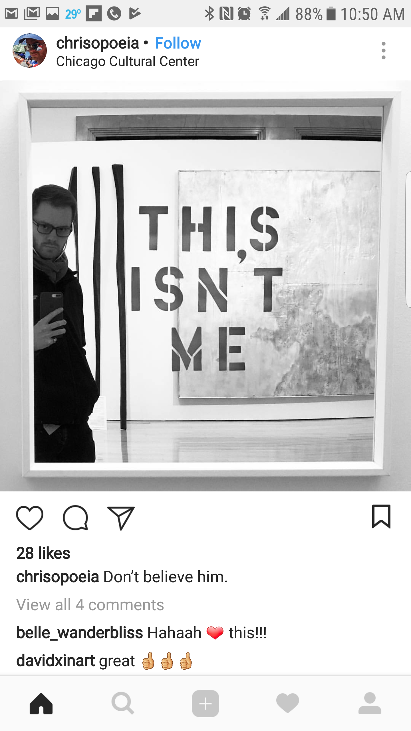 A man takes a selfie with a mirror at an art exhibit, capturing a wall with a large mixed-media artwork that reads "THIS ISN'T ME" in cut-out letters. Behind him, a large abstract painting is visible.
