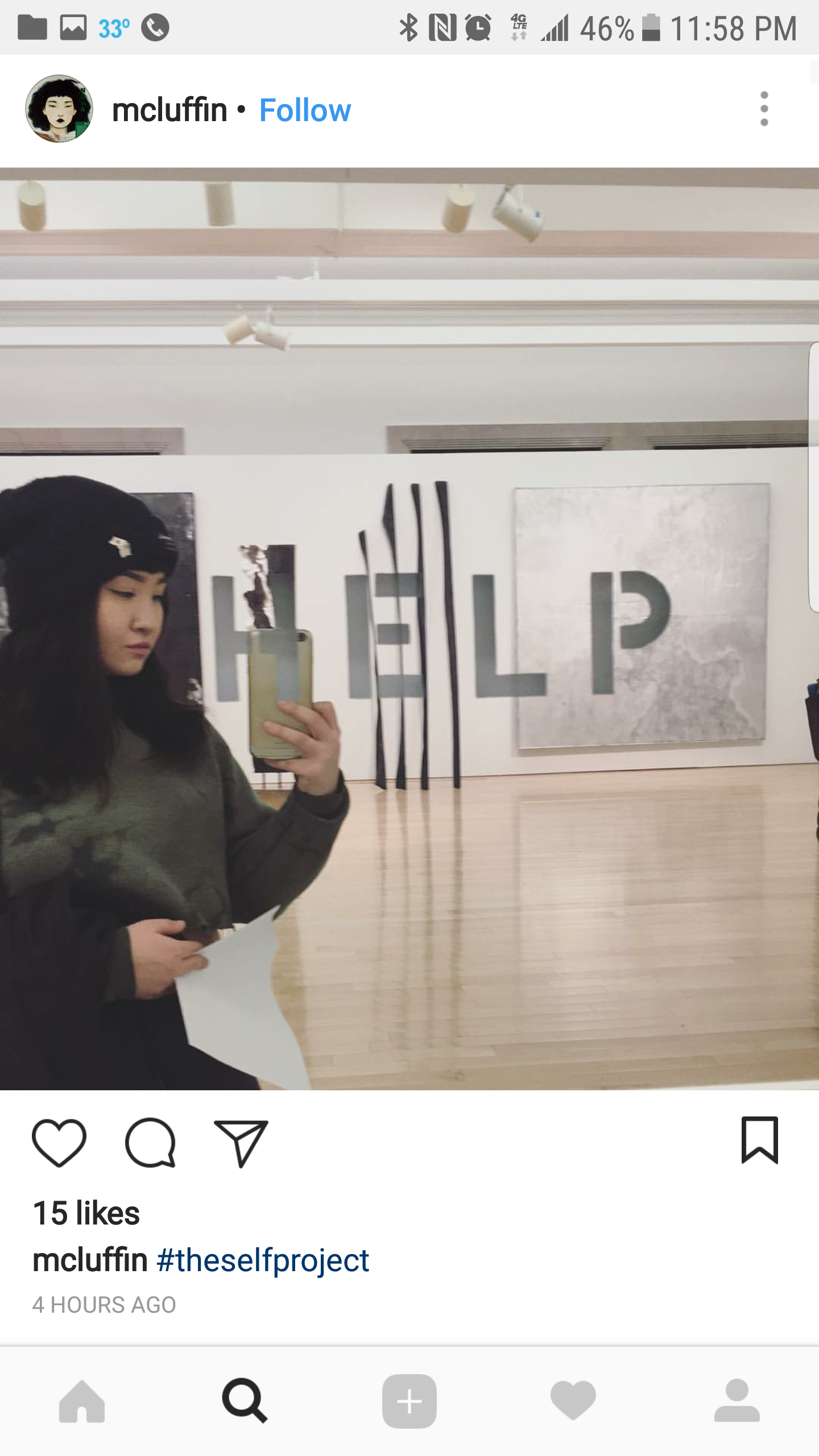 A woman taking a mirror selfie at an art gallery with the word 'HELP' displayed behind her, with the letters partially obscured by vertical black slats.