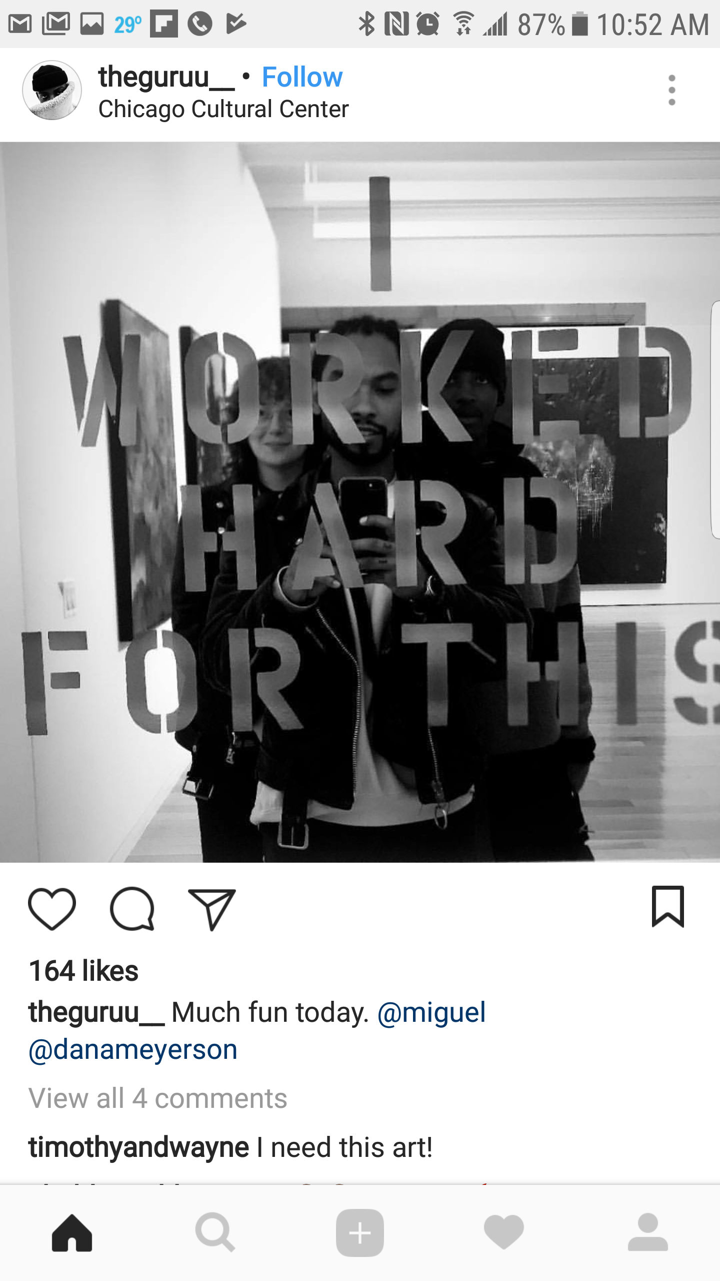 Black and white photo of three people taking a mirror selfie inside a museum or gallery, with text on the mirror that reads 'WORKED HARD FOR THIS'.