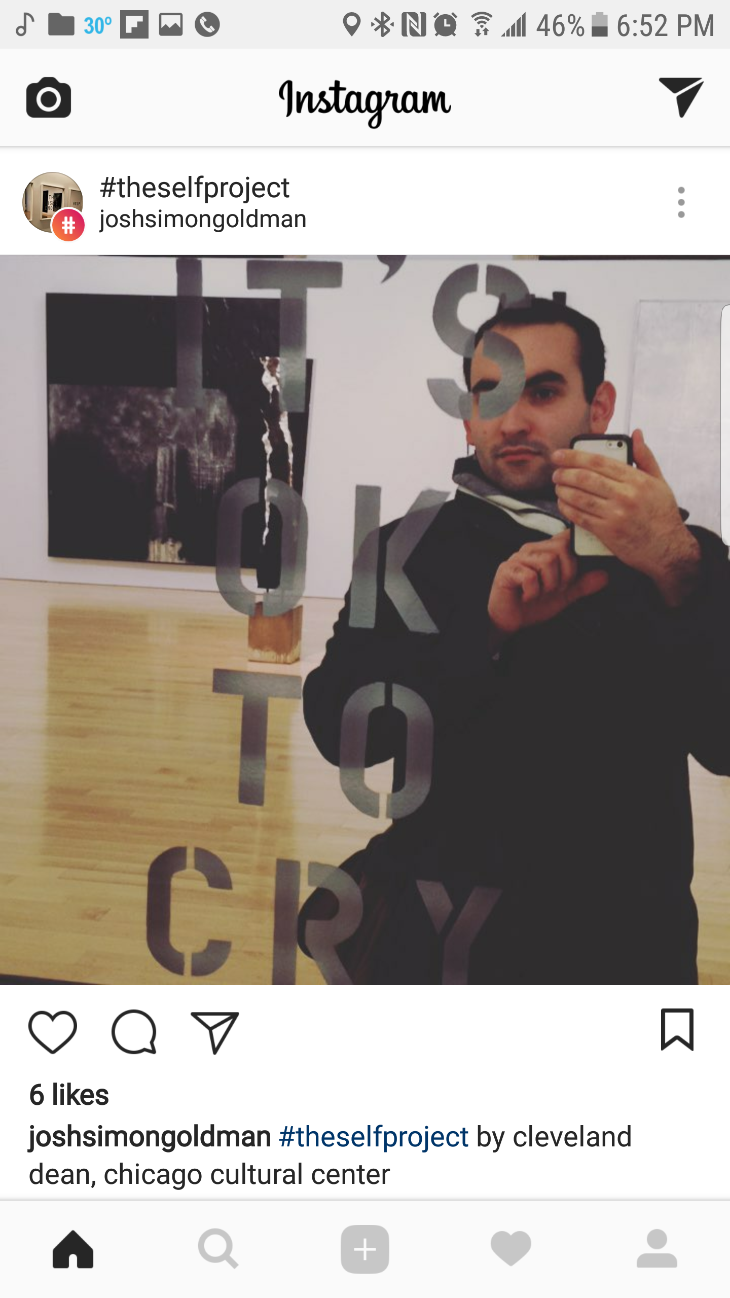 Self-portrait of a man taking a mirror selfie in an art gallery, with words written on the mirror that read 'PHOTO OF THE CITY'.