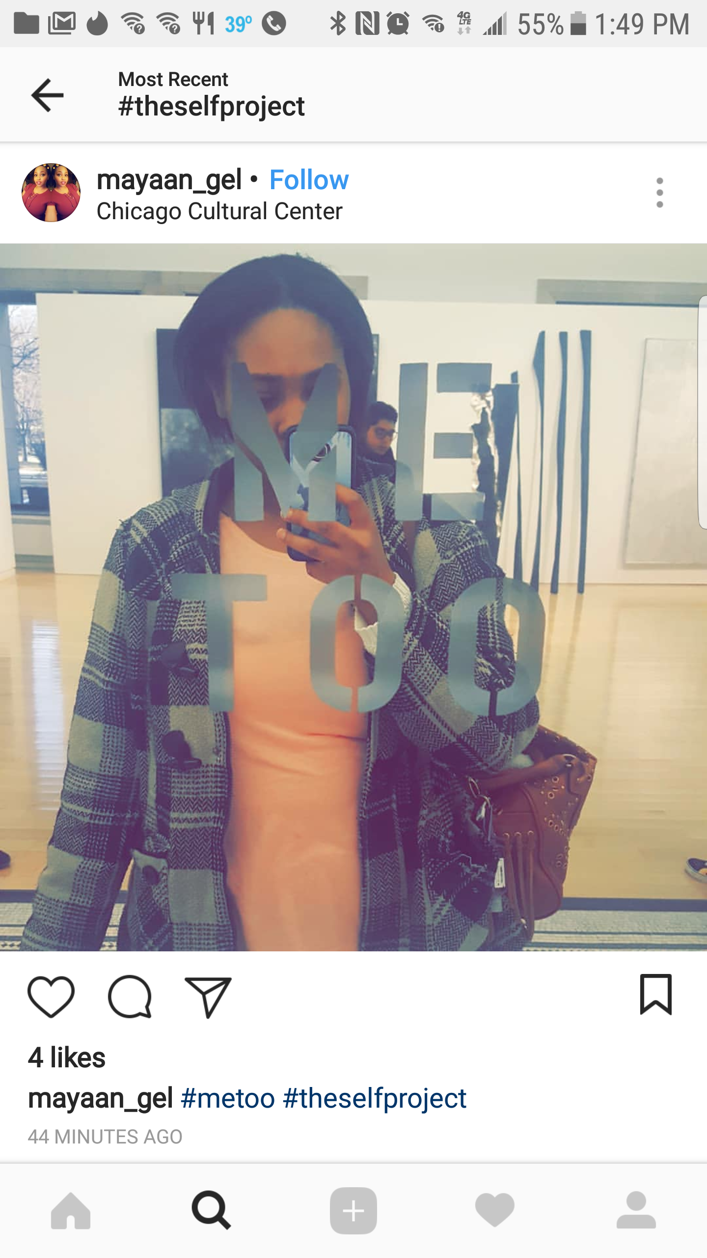 A woman taking a mirror selfie at the Chicago Cultural Center, with her phone covering part of her face. She is wearing a patterned coat over a blush-colored top, and there is a large text on the mirror that reads 'ME TOO.'
