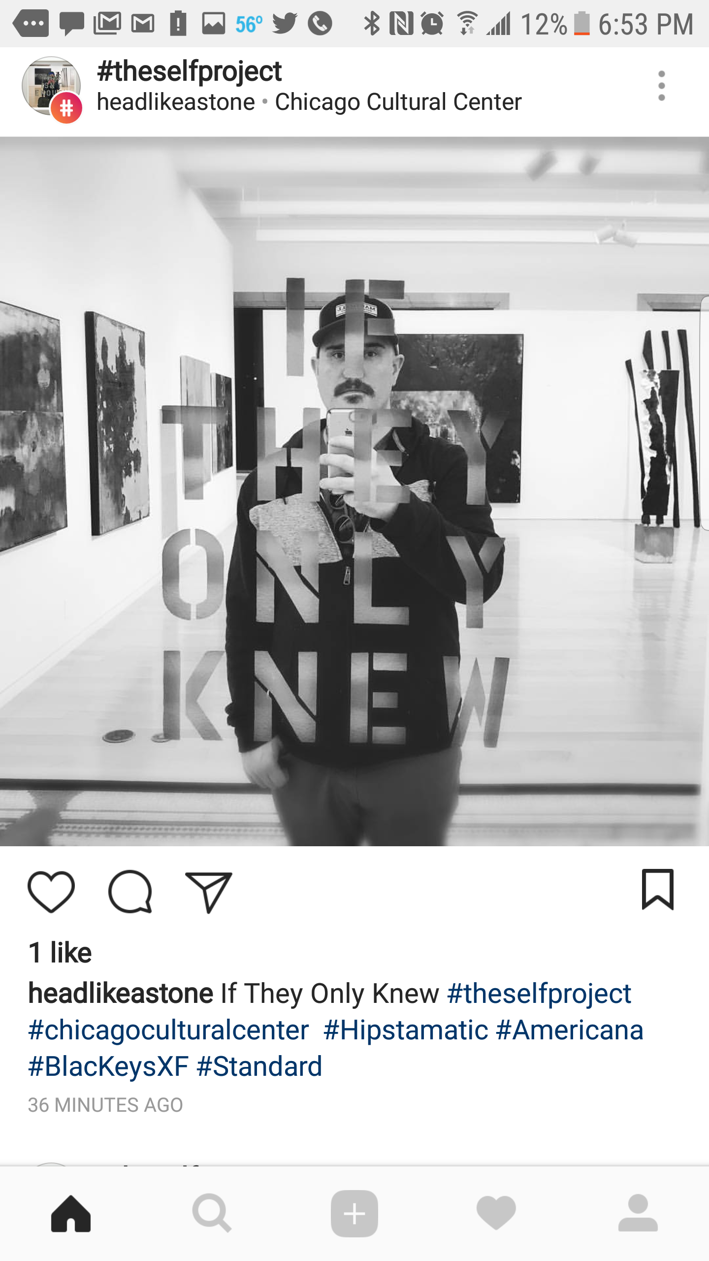 Black and white photo of a man taking a selfie in an art gallery with paintings displayed on the walls. The gallery has the phrase 'If They Only Knew' written on a glass wall in front of the man.