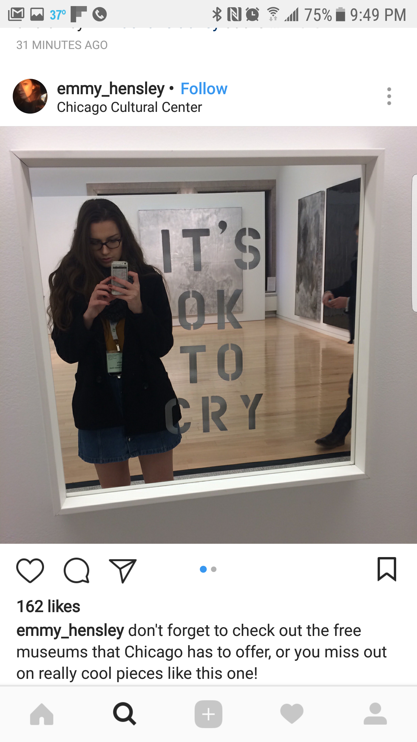 A woman taking a mirror selfie at the Chicago Cultural Center, with a quote on the mirror that reads "IT'S OK TO CRY." In the background, there are artworks on the gallery walls.