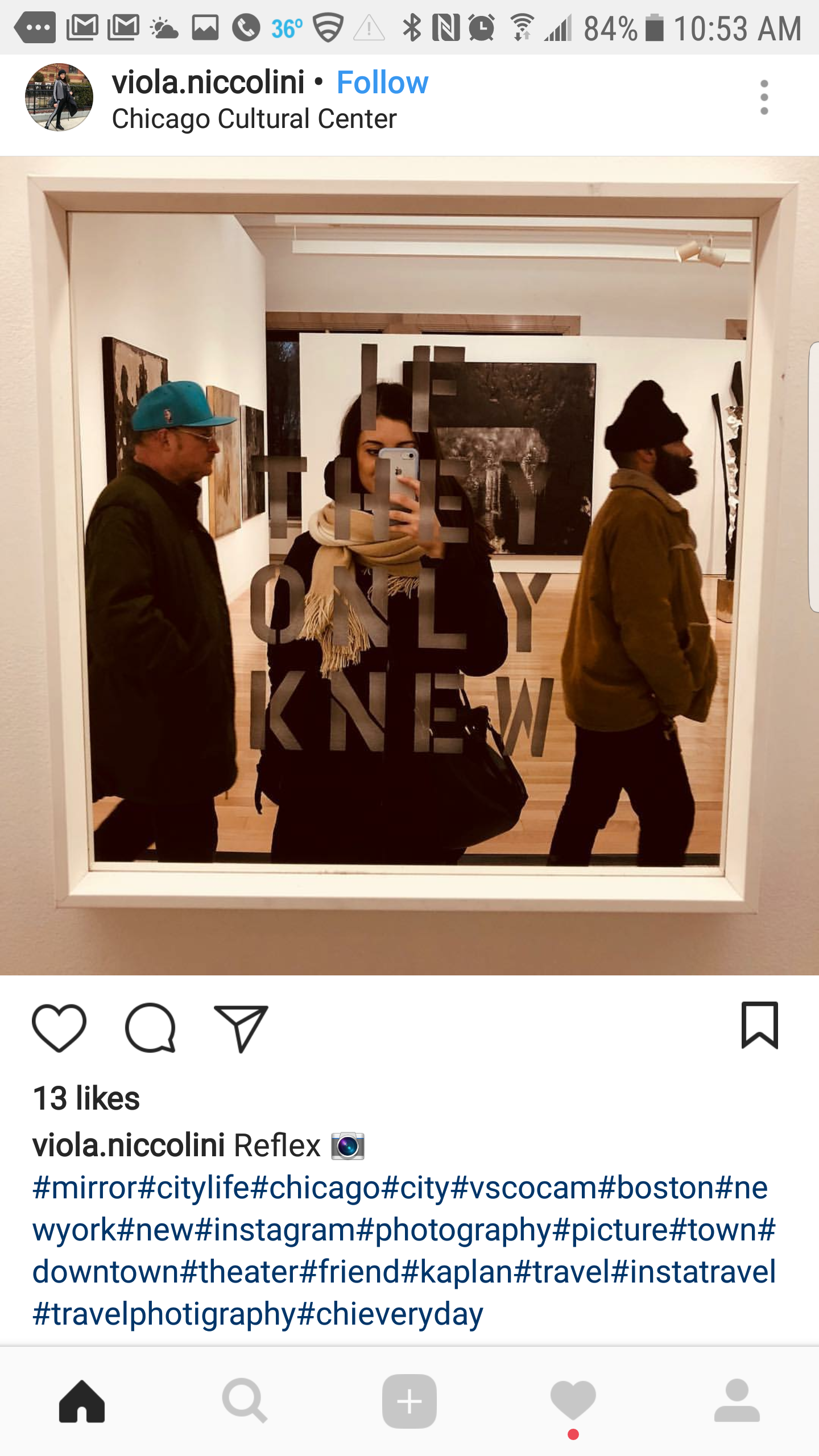 A woman taking a selfie in a mirror at the Chicago Cultural Center, with two men walking by in the background.