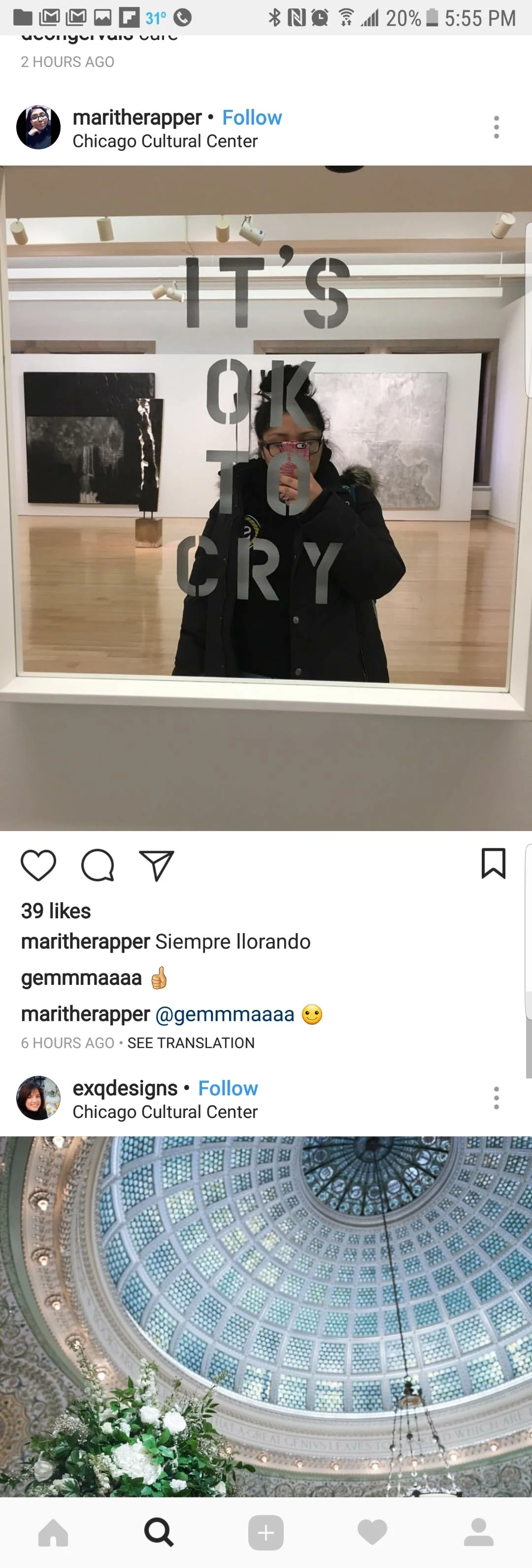 A woman taking a mirror selfie at an art gallery with the quote 'It's okay to cry' written on the mirror, with artworks visible in the background.