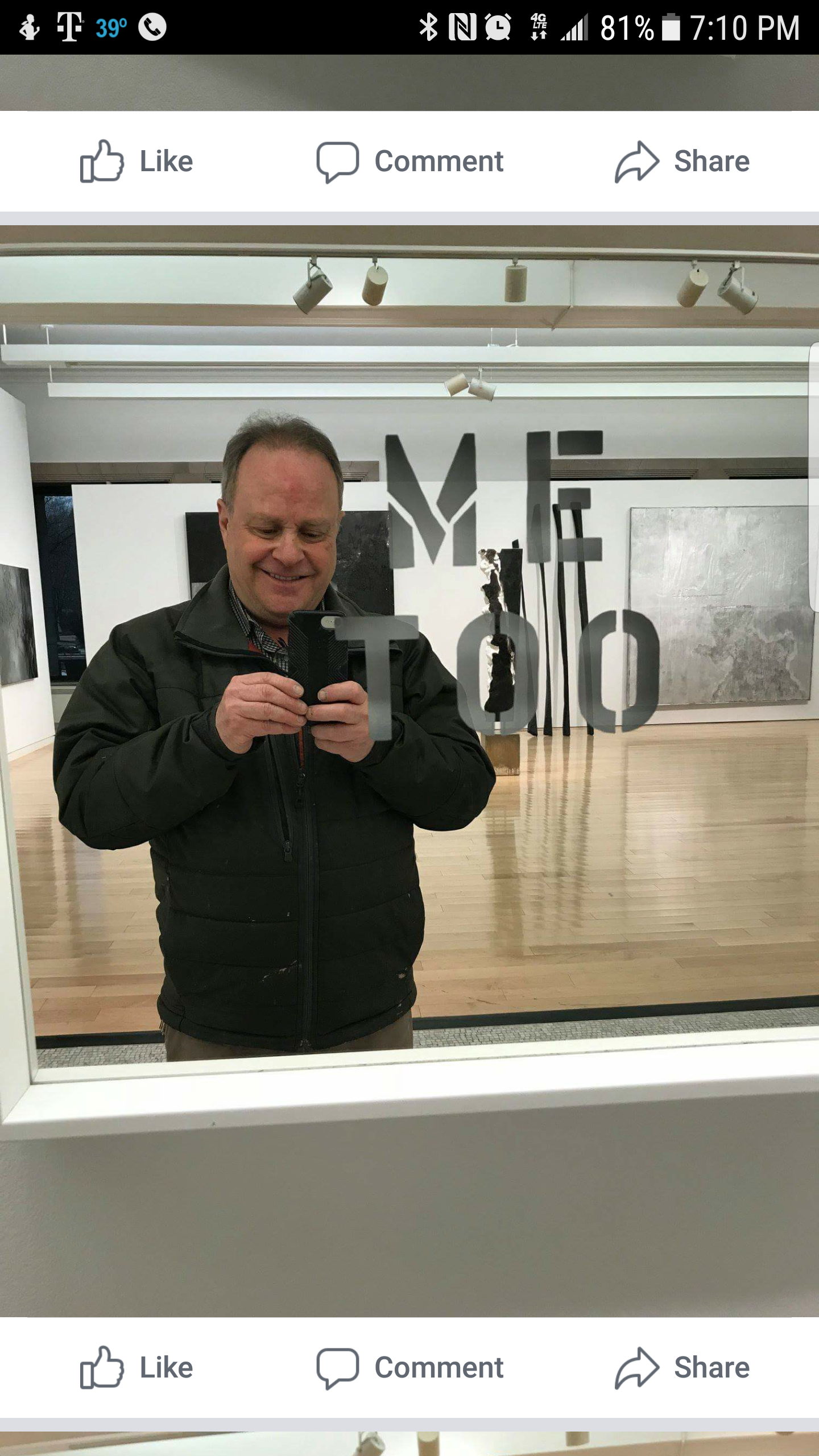 A man taking a selfie in an art gallery mirror with the word 'METRO' reflected on the glass, and artwork and sculptures visible in the background.