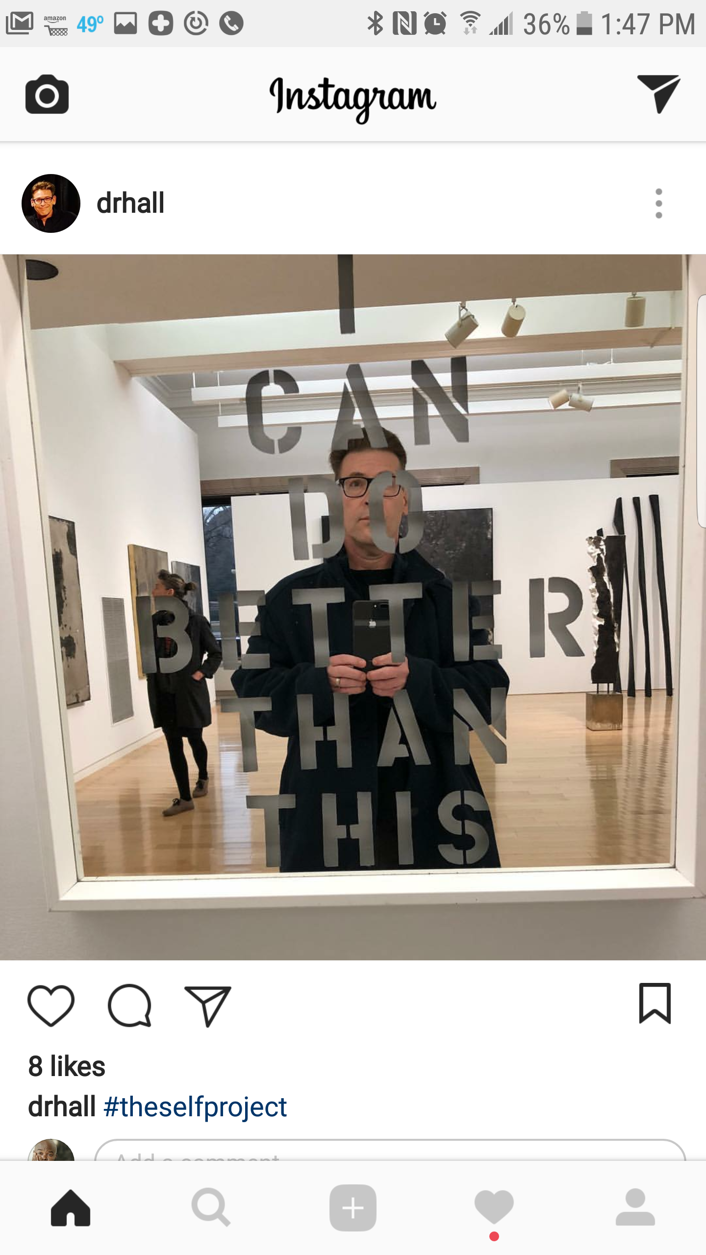 A man taking a selfie in a museum mirror with the words 'I CAN DO BETTER THAN THIS' written on the mirror. Art pieces are visible in the background.
