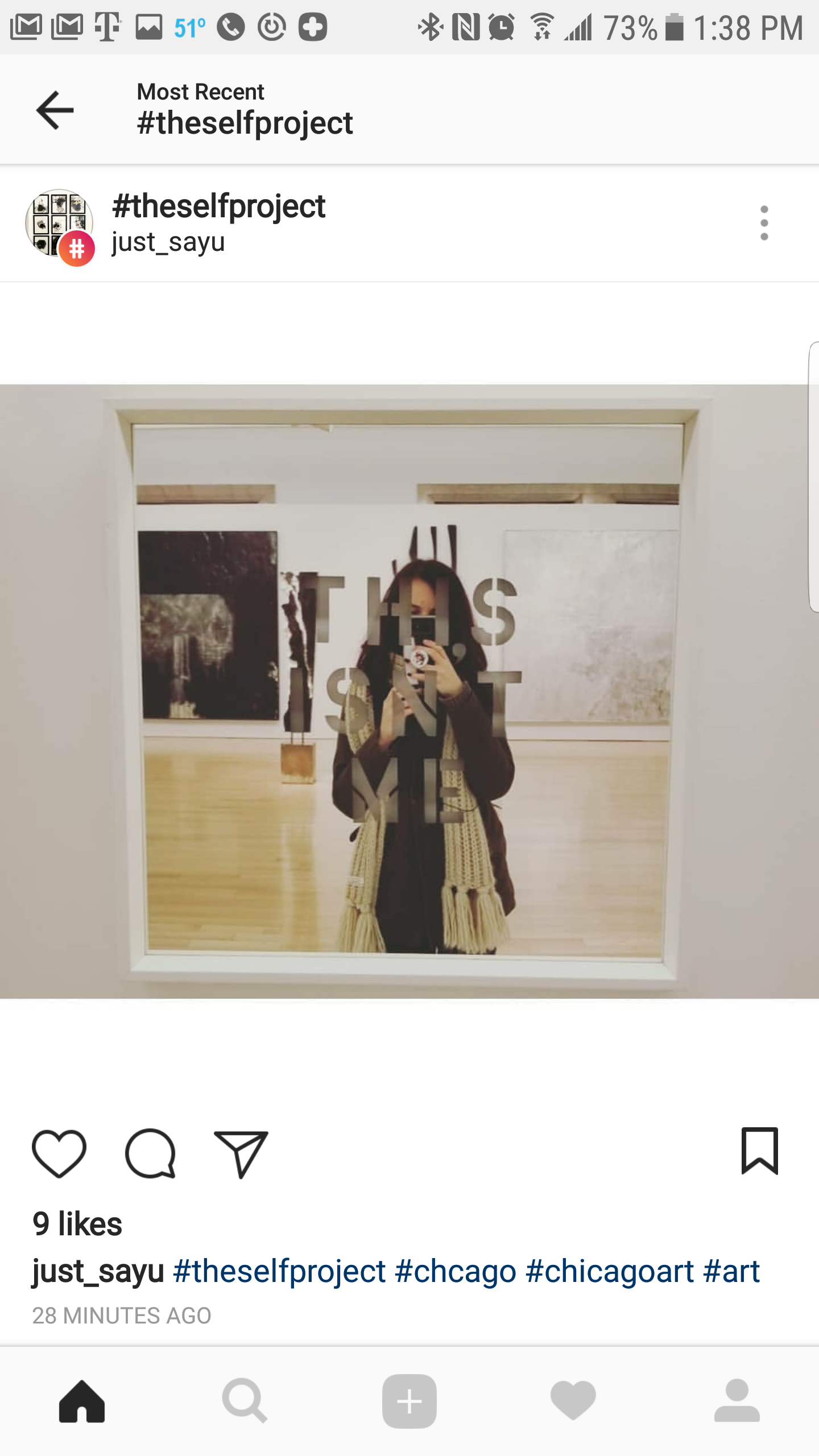 A person taking a selfie mirror reflection at an art gallery, with black lettering on the glass that says 'THIS IS ART.'