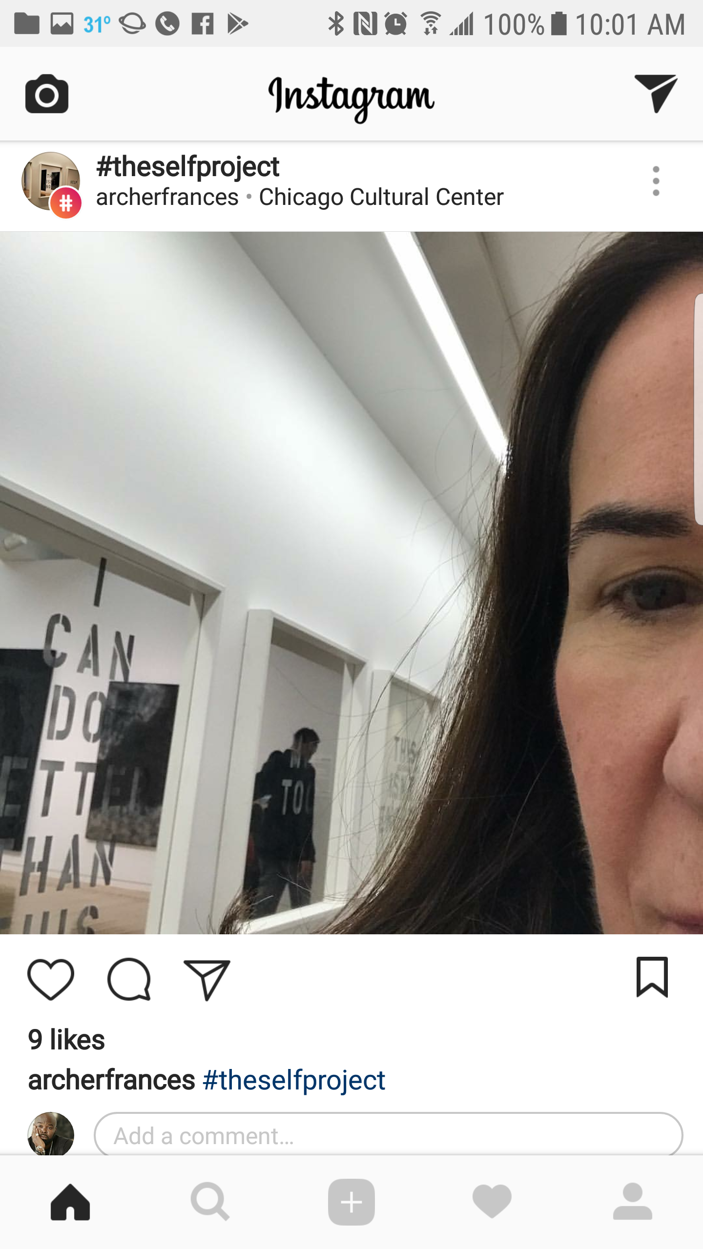 Close-up of a woman's face partially visible on a photo taken inside an art gallery or museum. In the background, there are framed artworks and a person looking at the art.