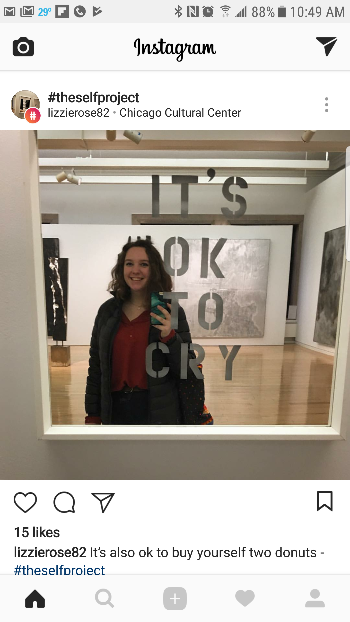 A young woman taking a mirror selfie in an art gallery with the words 'IT'S OK TO CRY' on the mirror.