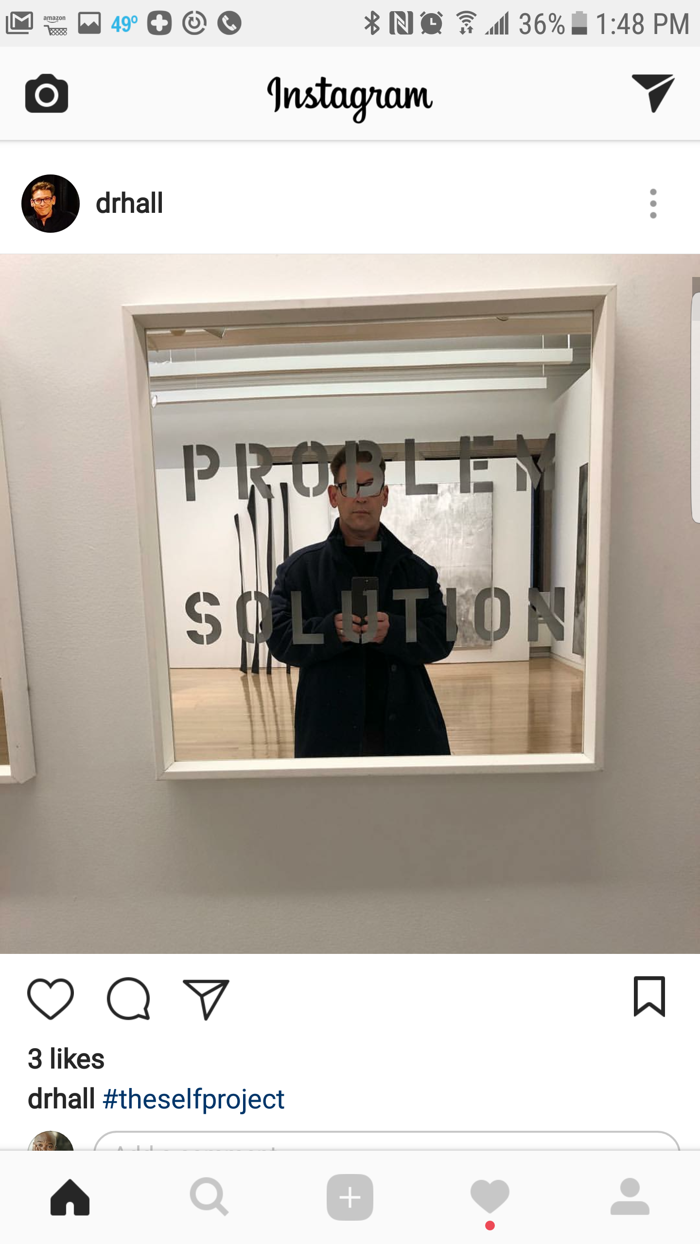 A man taking a selfie in a mirror with the words "PROBLEM SOLUTION" written on it. The mirror is part of an art display or installation with hanging wands or tools in the background.