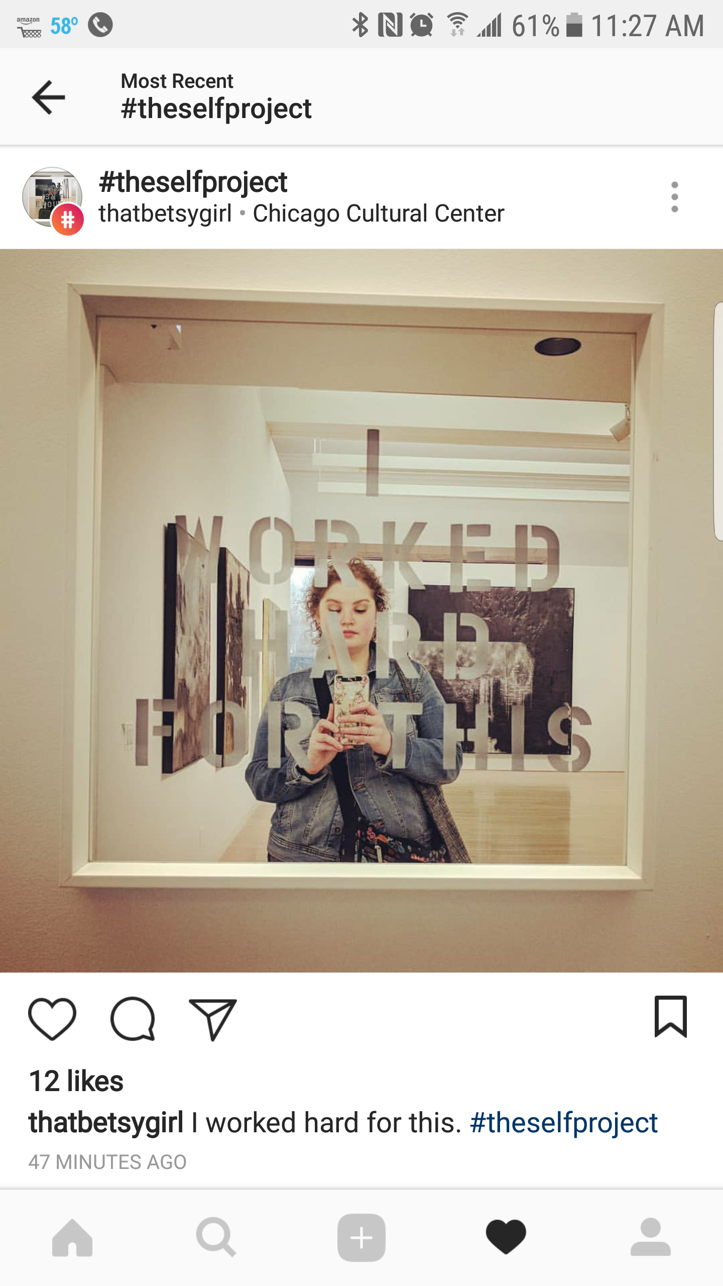 A woman taking a mirror selfie in an art gallery, with the words 'I WORKED HARD FOR THIS' written on the glass of the mirror.