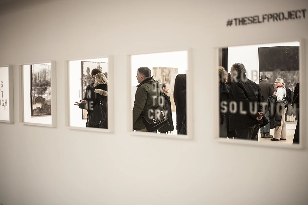 View through a museum window showing people looking at artwork inside the gallery.