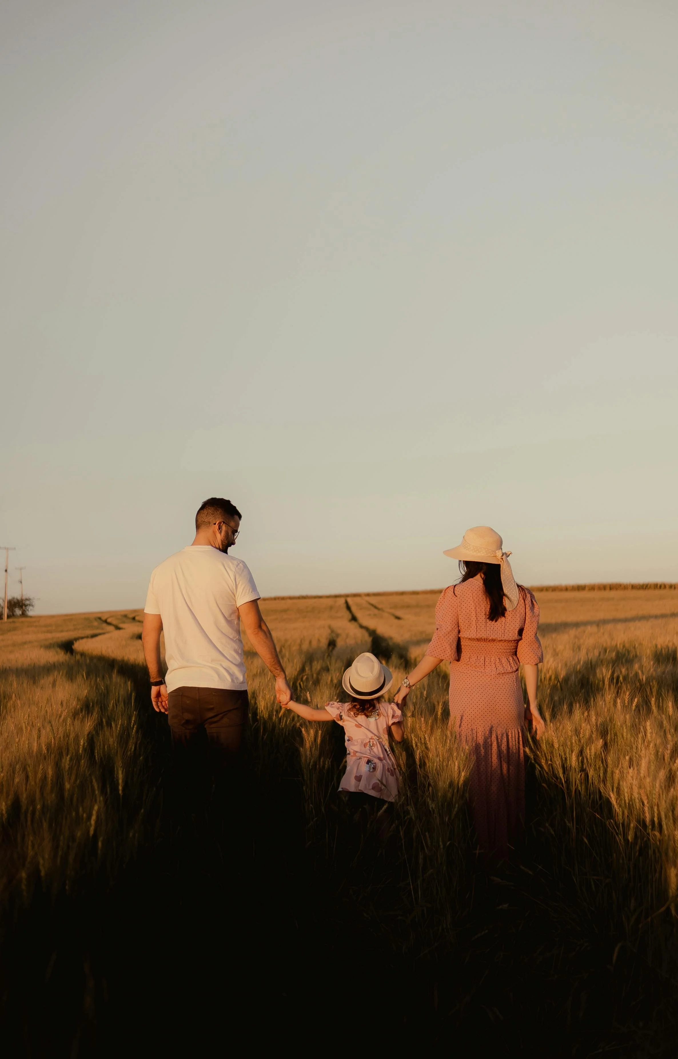 A family of four, including a man, woman, and two children, walking hand in hand through a field during sunset.