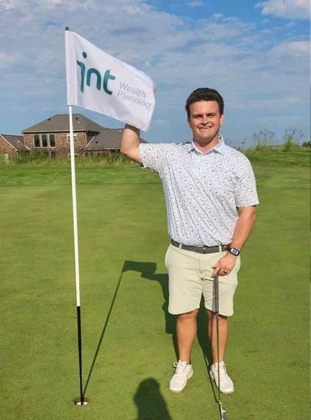 Rob Clark on a golf course holding an INT Wealth Planning flag