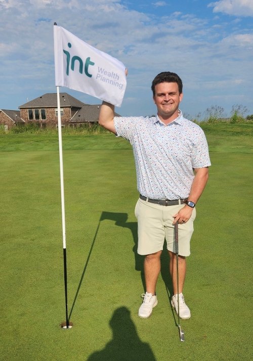 Rob Clark standing in front of a INT Wealth Planning golf flag