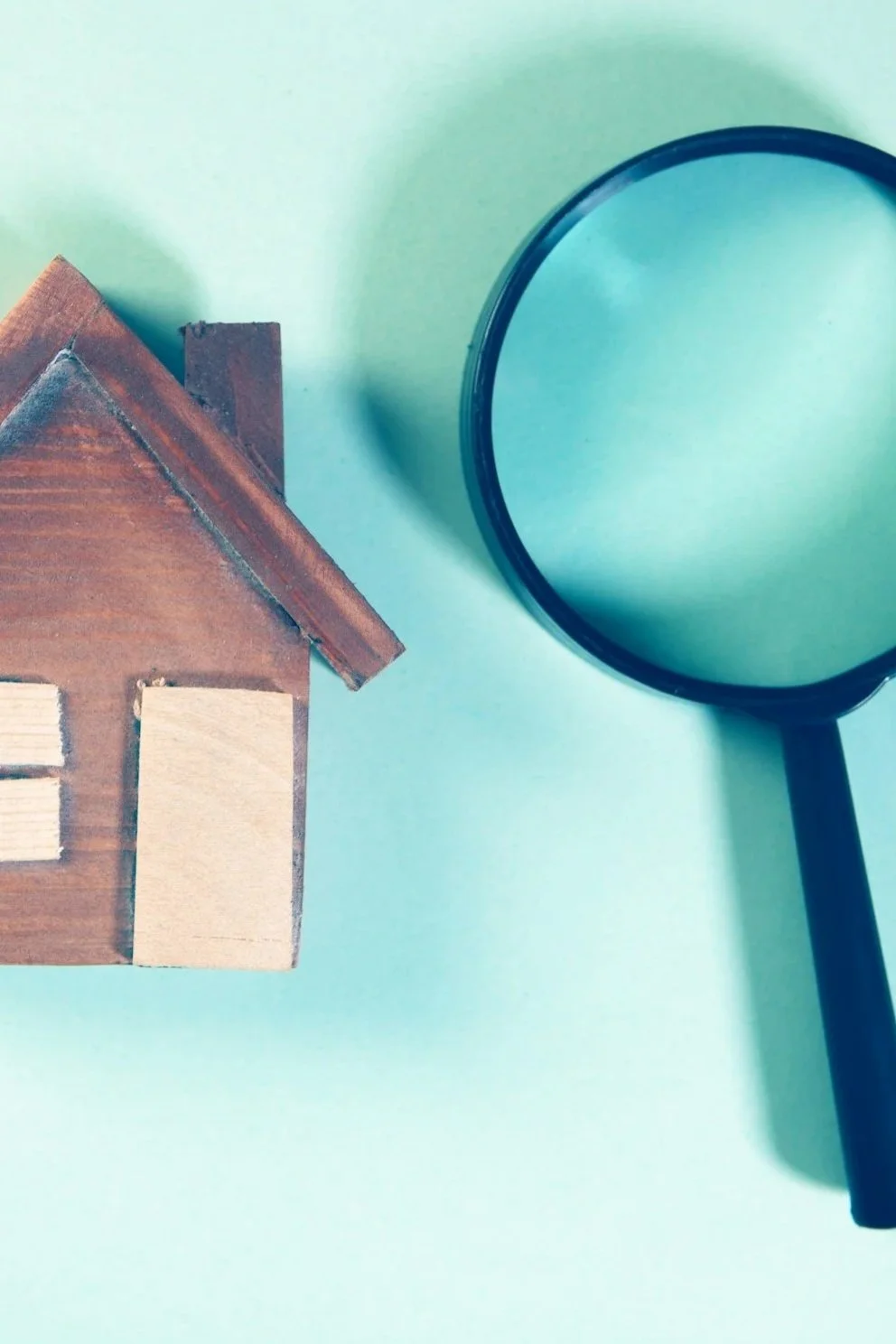 A small wooden house model and a magnifying glass on a light green surface.