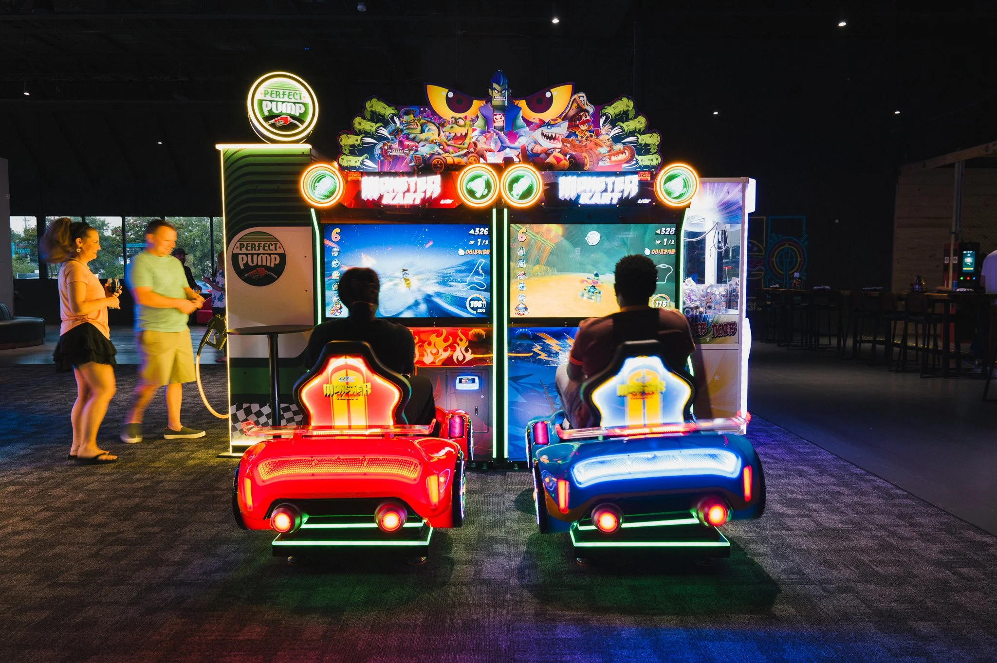 People playing arcade games in a dimly lit arcade with colorful neon lighting.