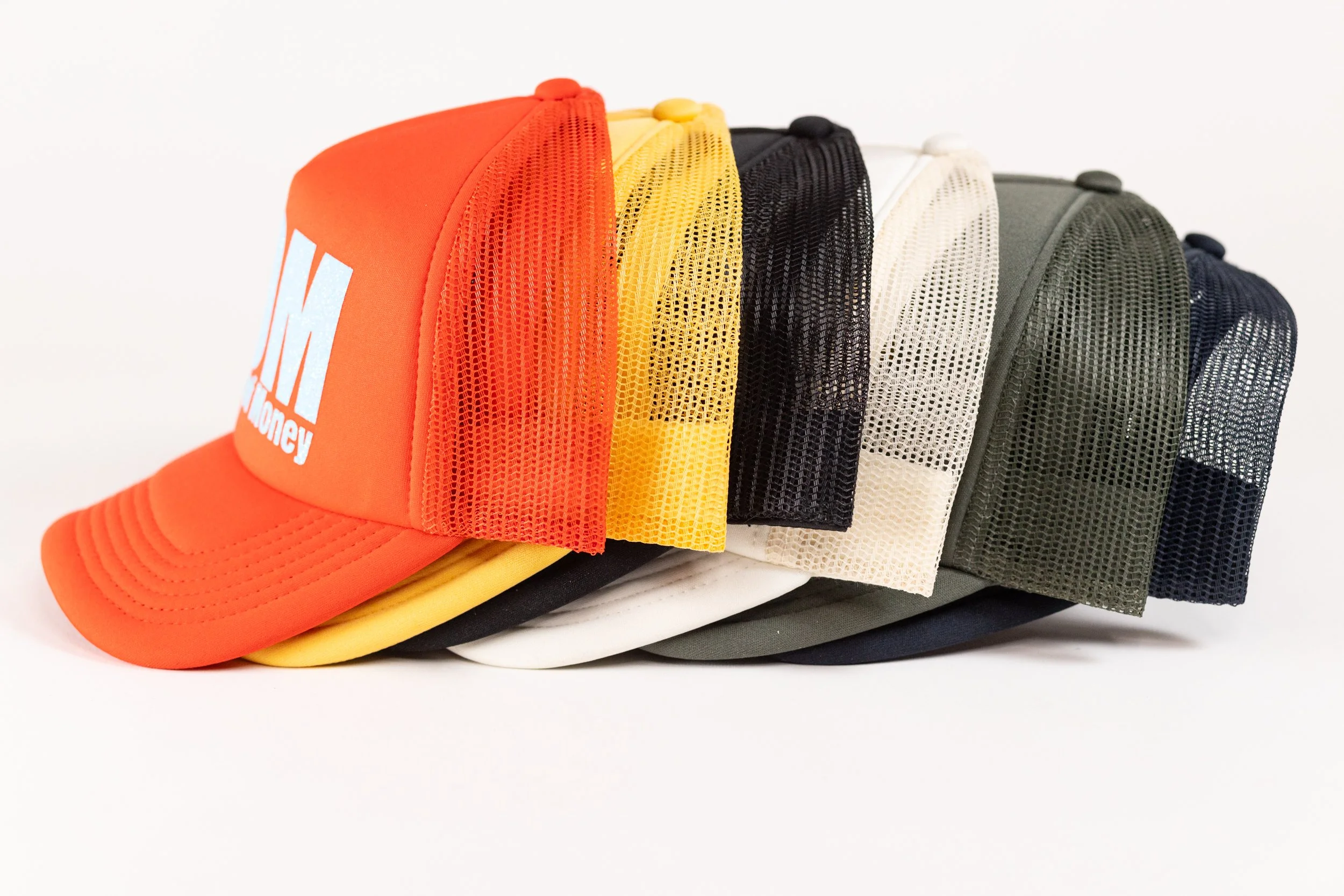 A collection of six colorful mesh trucker caps stacked together, including orange, yellow, black, white, green, and navy blue.