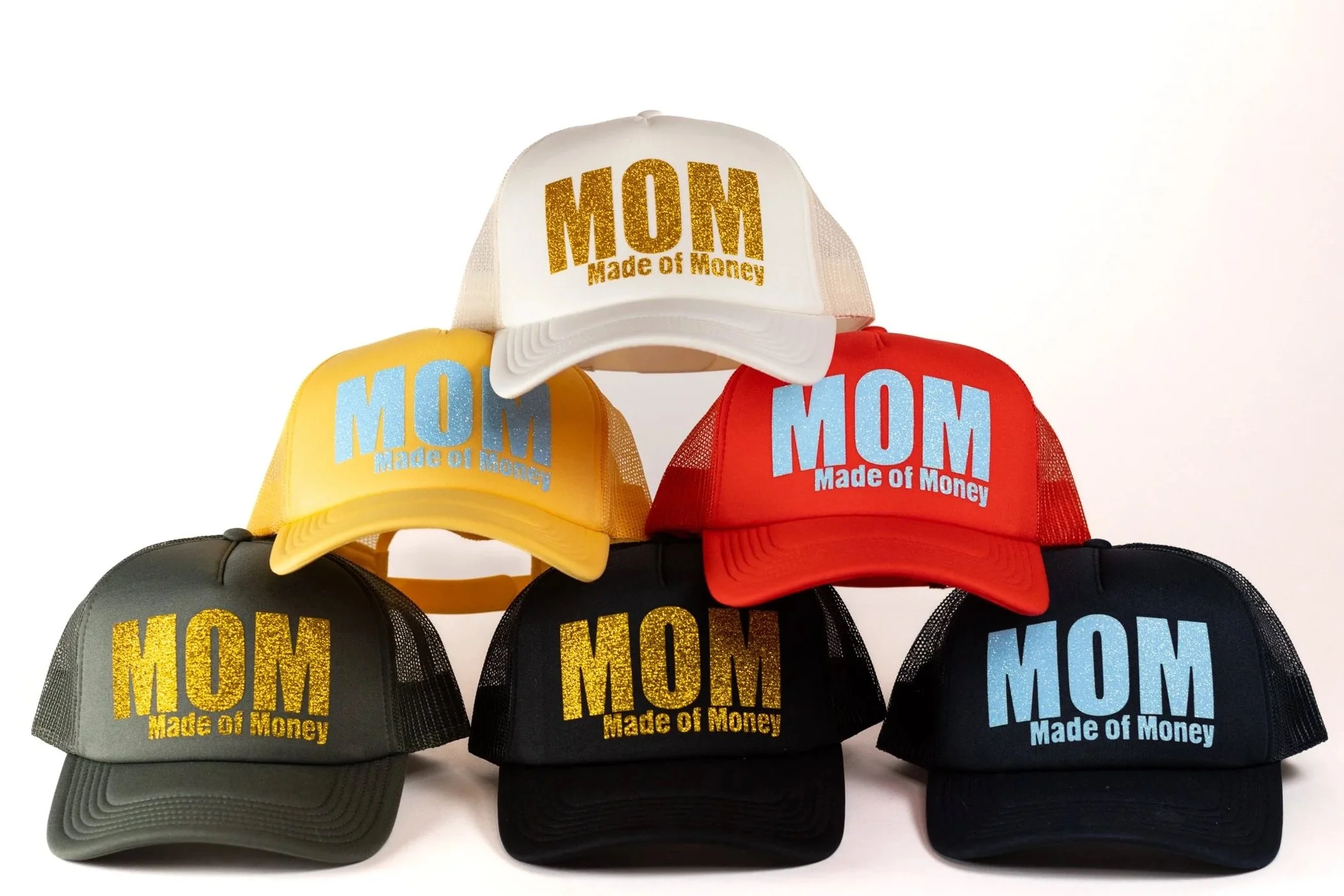 Collection of six trucker hats with the phrase 'MOM Made of Money' in glittery and bold text, in white, yellow, red, gray, black, and navy colors.