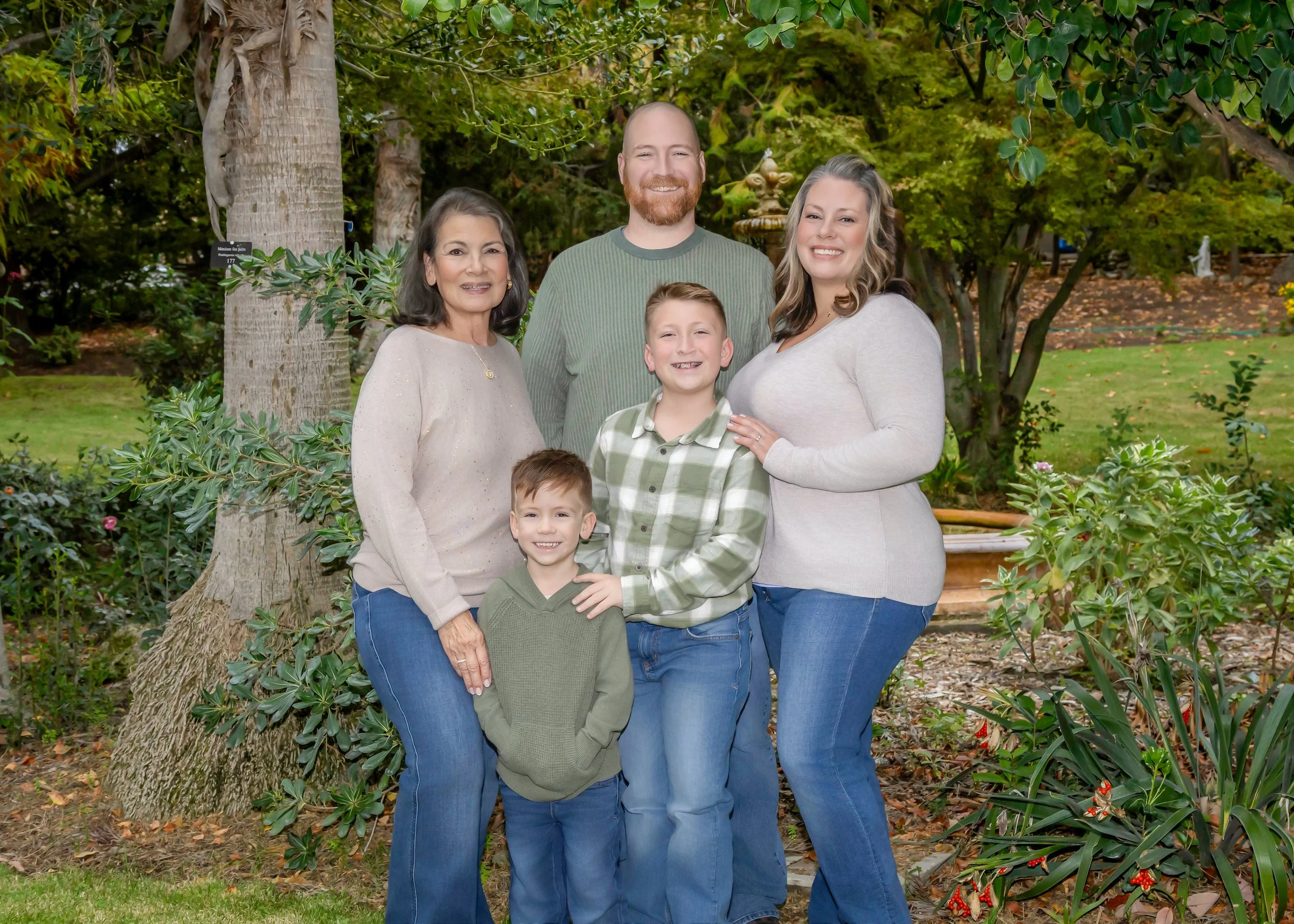 A multigenerational family of six standing outdoors in front of trees, smiling at the camera.