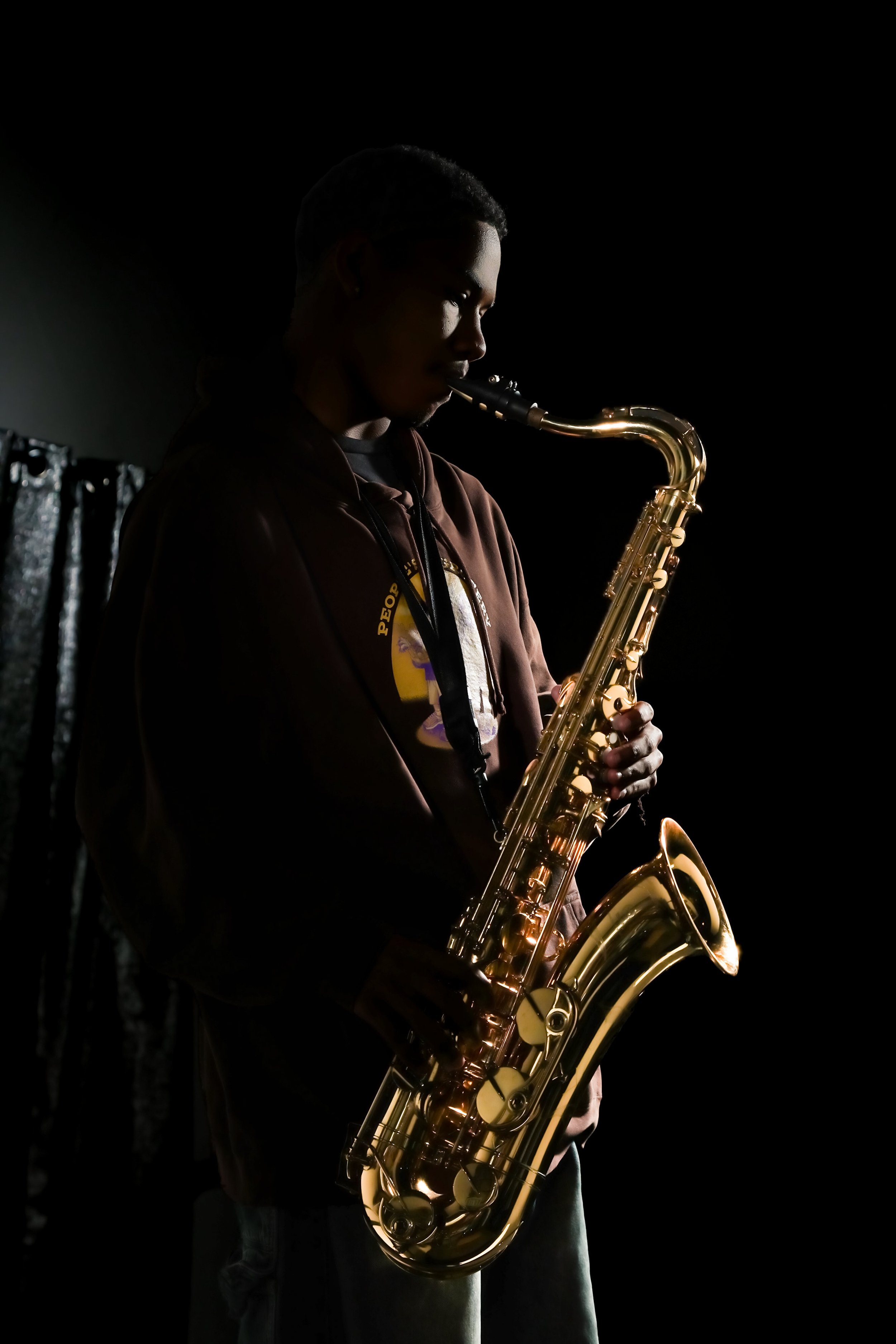 Person playing saxophone in a dark setting, with light highlighting the instrument and face.