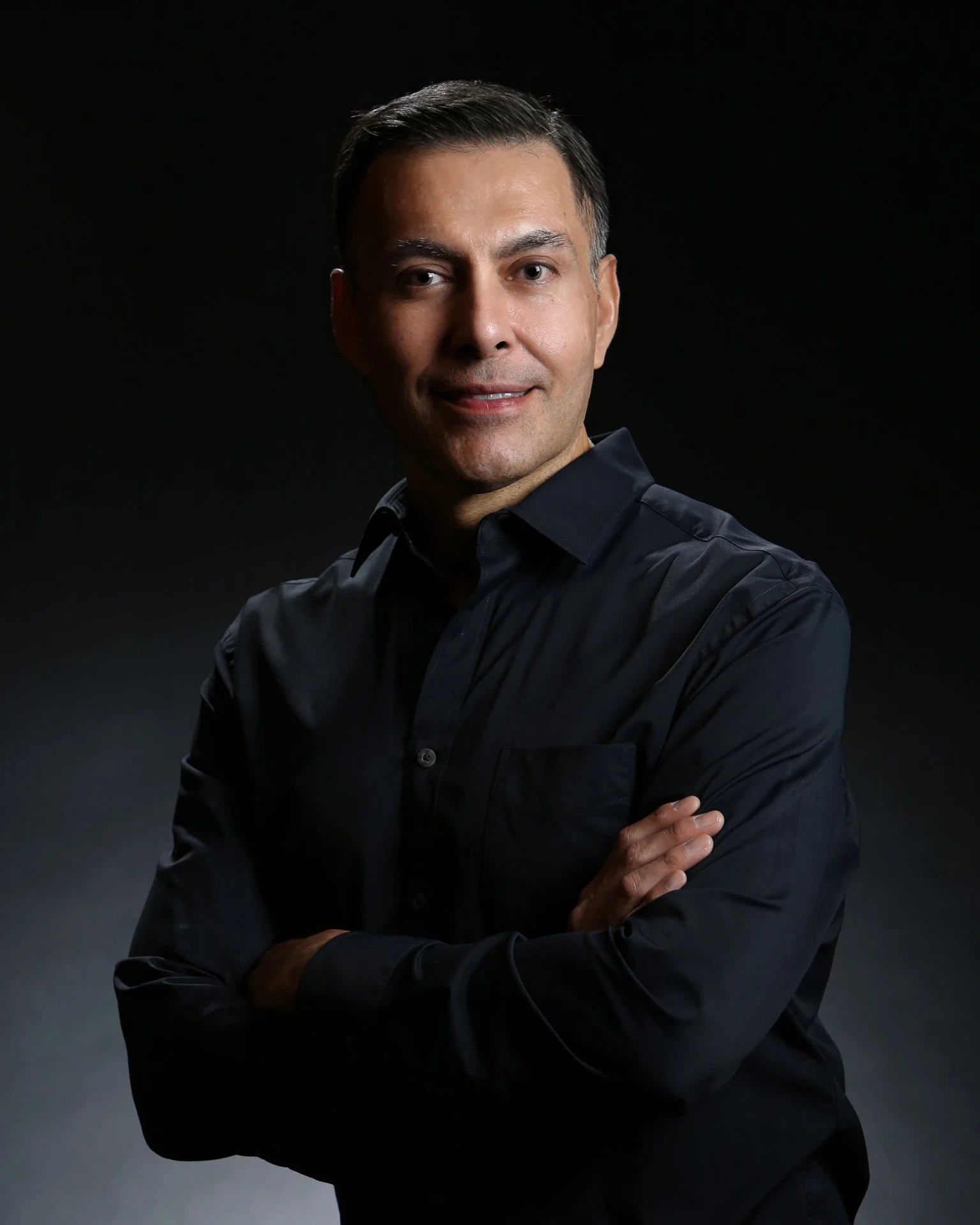 moody and dramatic headshot of a man crossing arms on a black background. 
