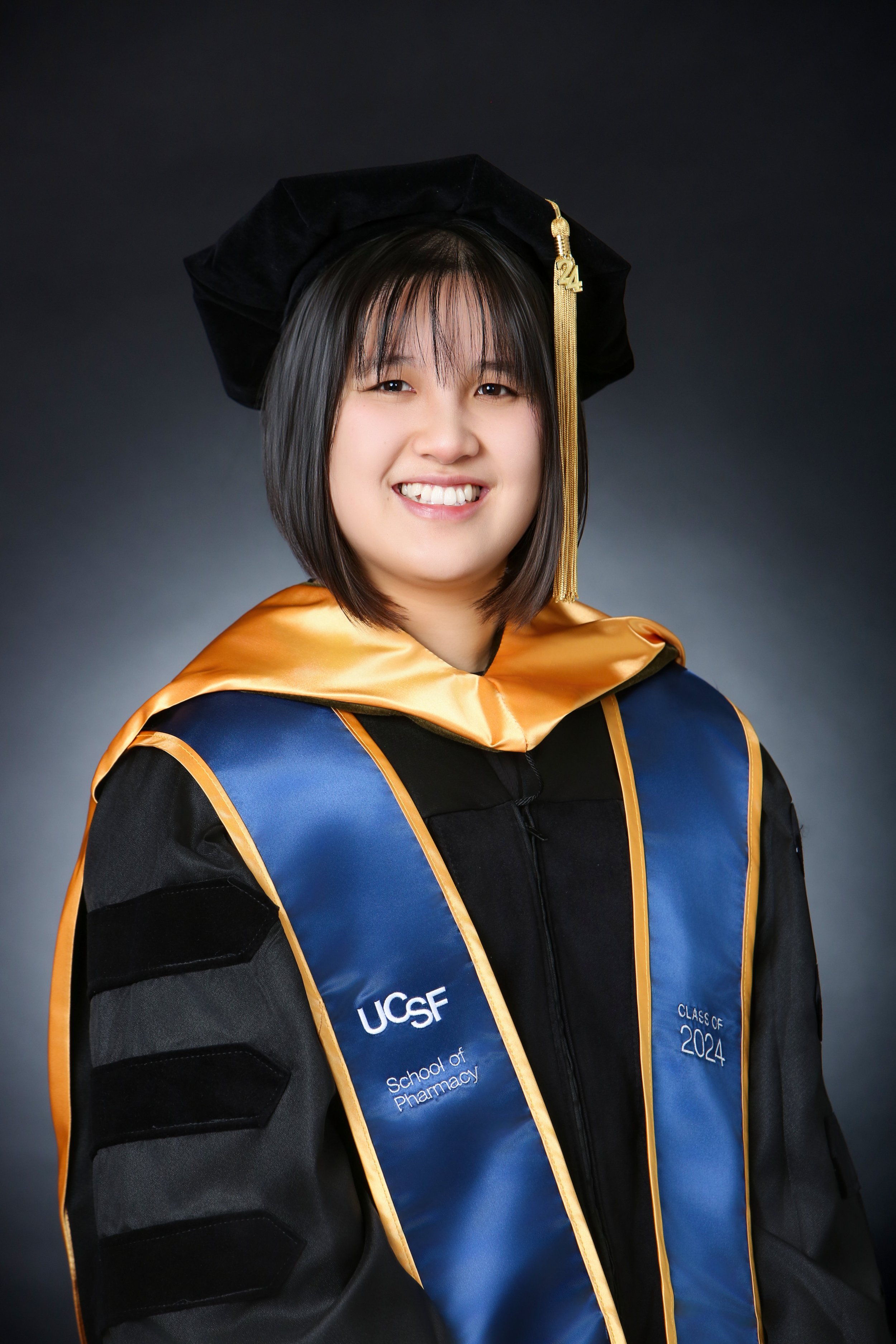 female masters graduate in traditional cap and gown in studio setting on black background