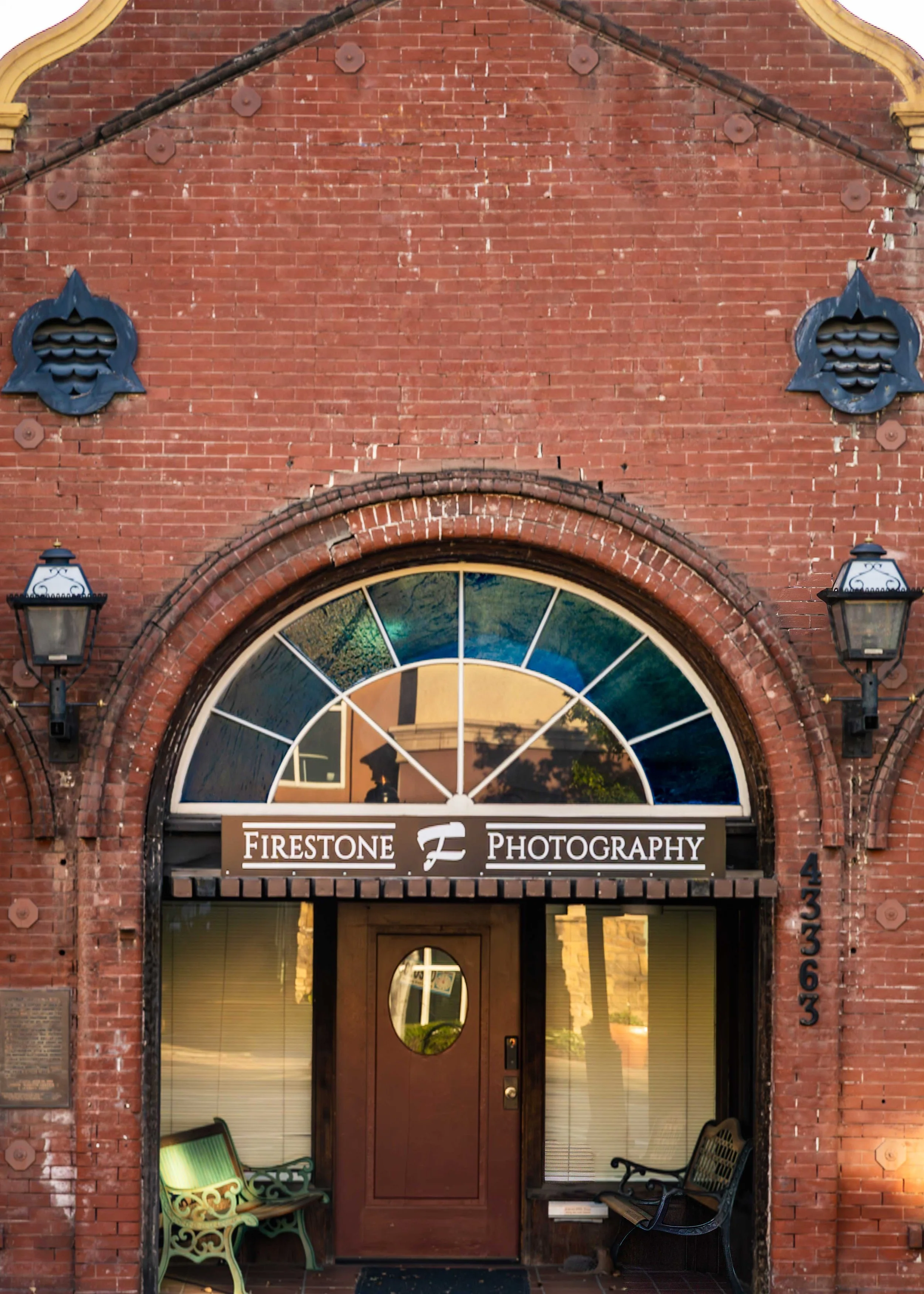 Brick building entrance with a wooden door, arched window above it, and a sign that reads 'Firestone Photography'.