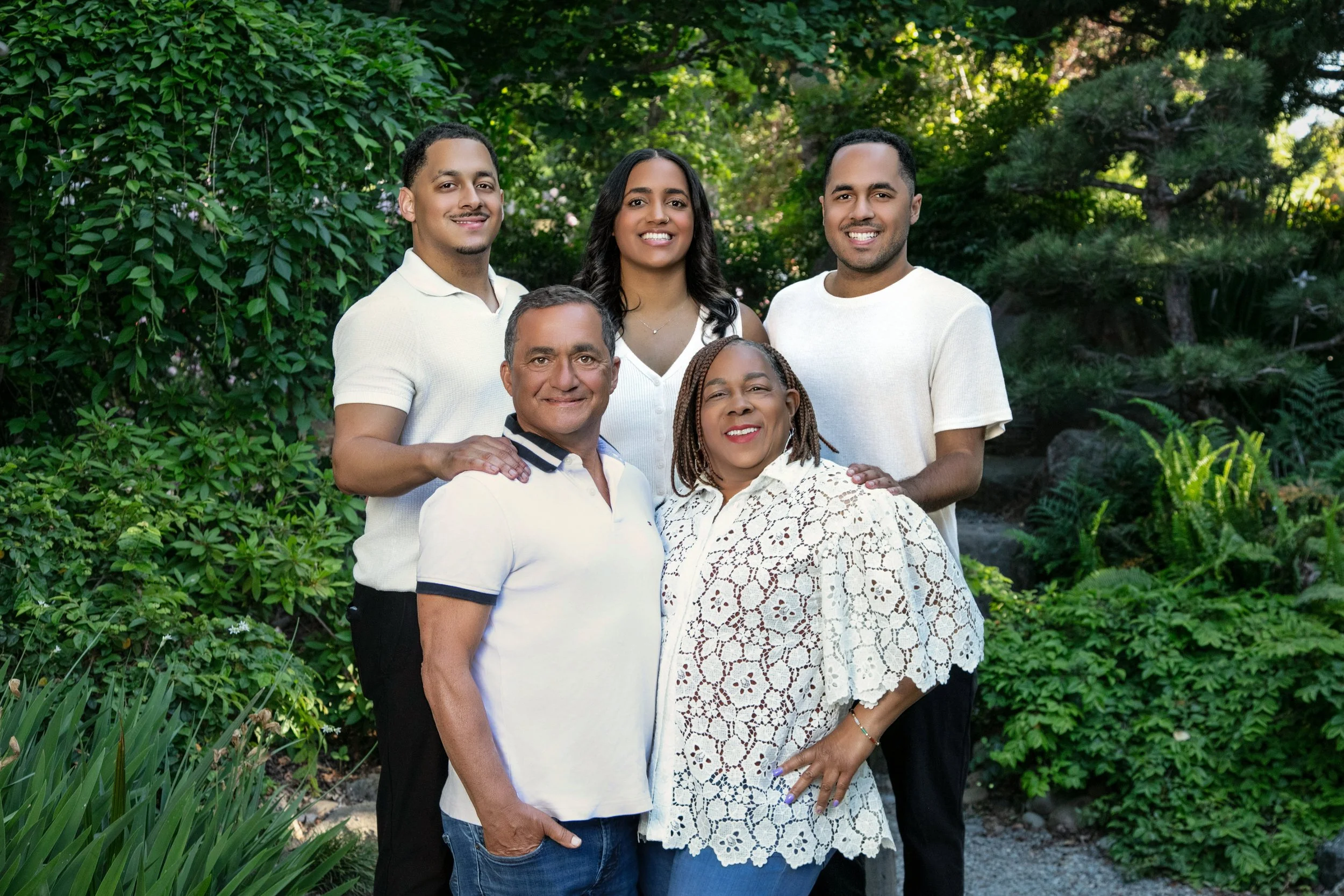 Group of five diverse people smiling outdoors in a lush green garden.