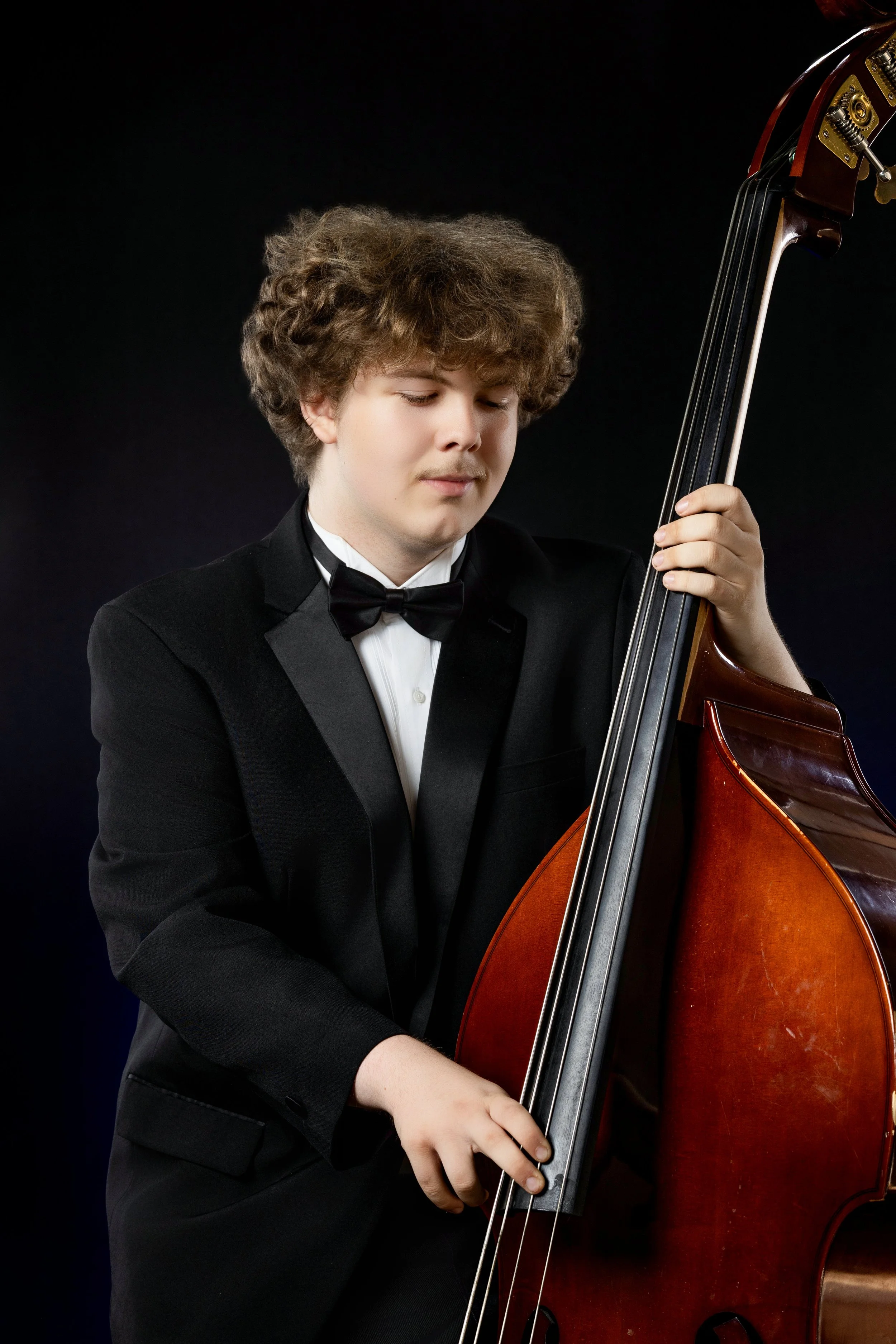 elegant high school senior boy with tuxedo playing the bass in studio with black background