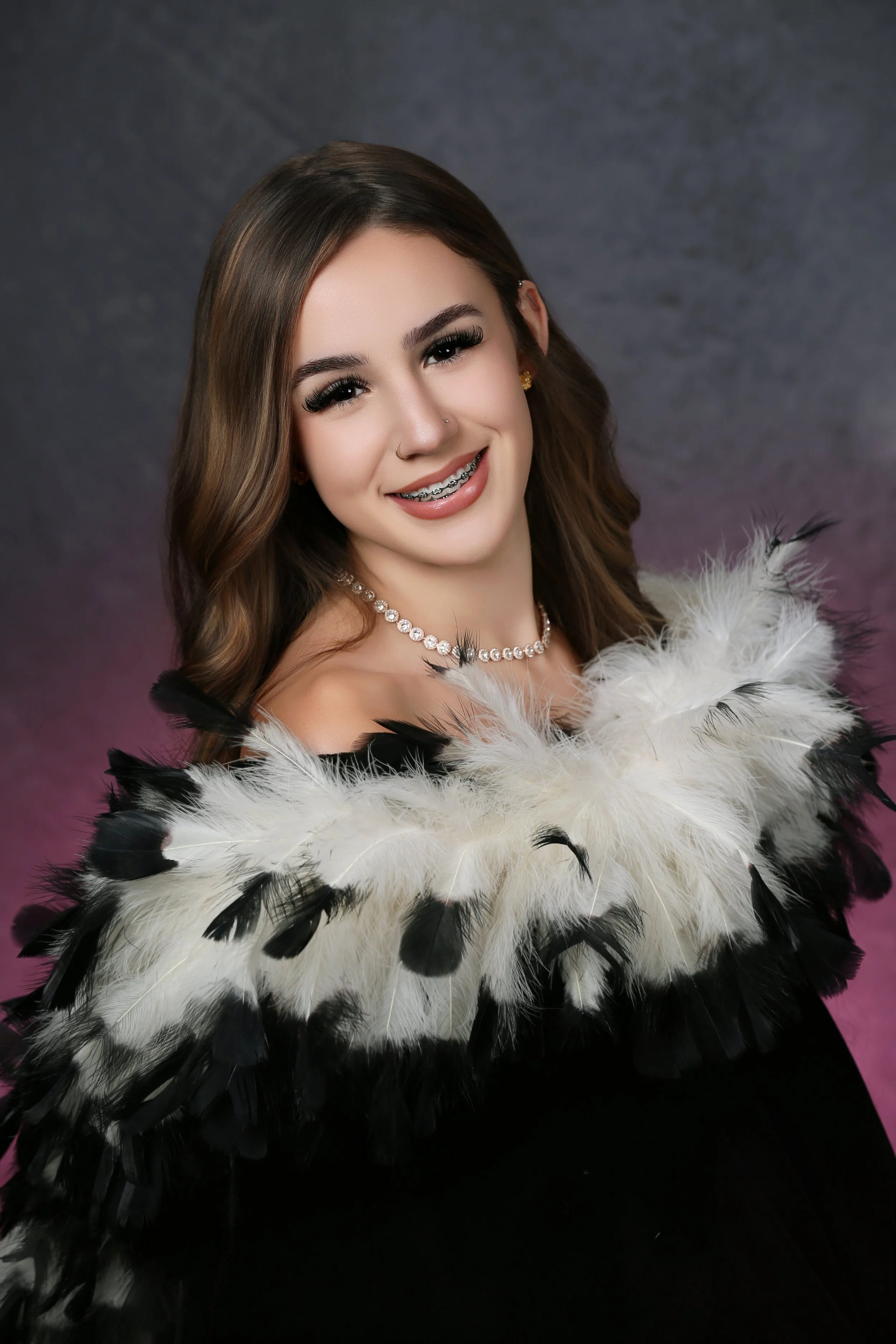 high school senior girl with feather drape in studio with pink and gray background
