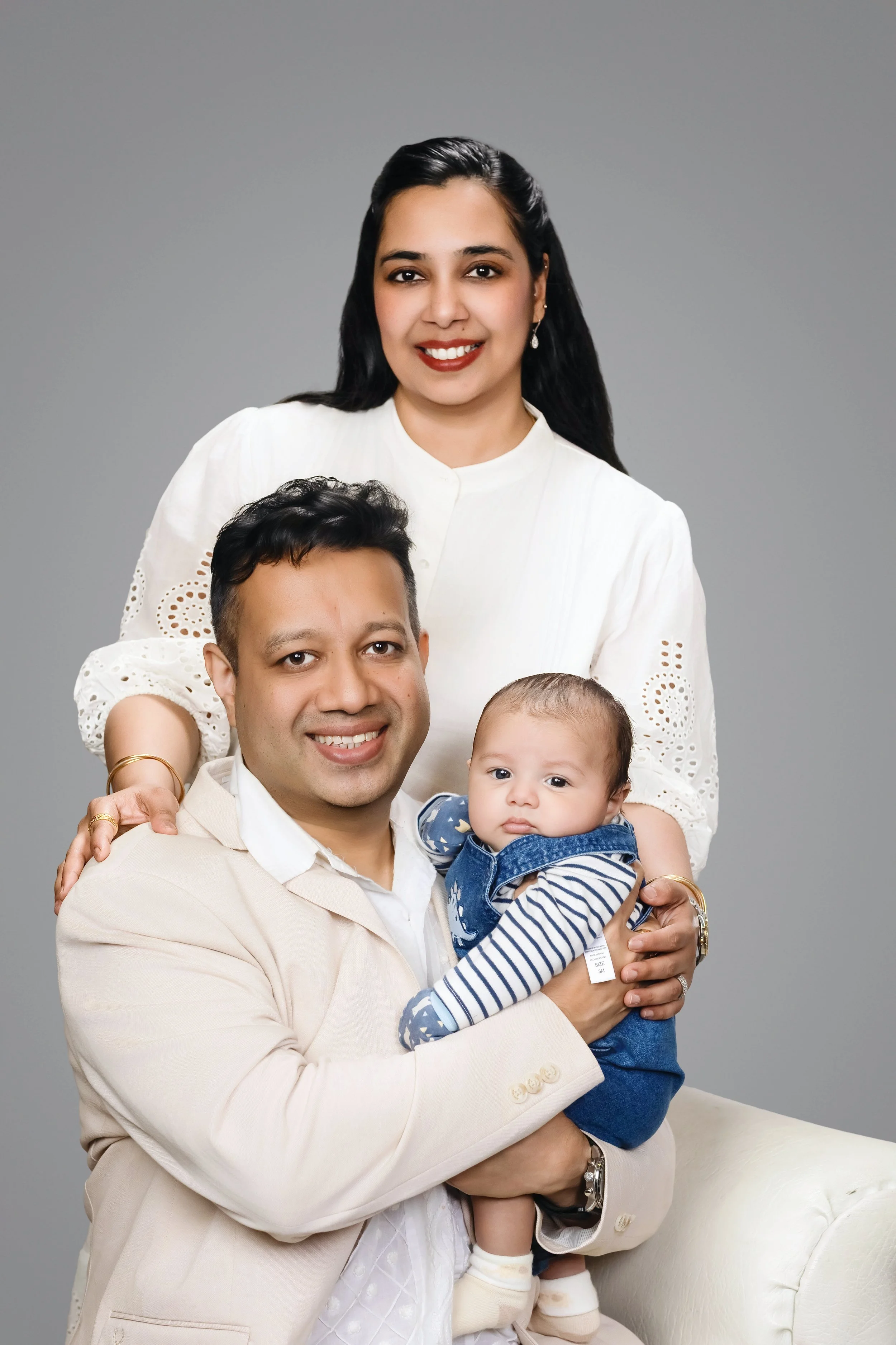family portrait of parents with baby in studio on gray background.
