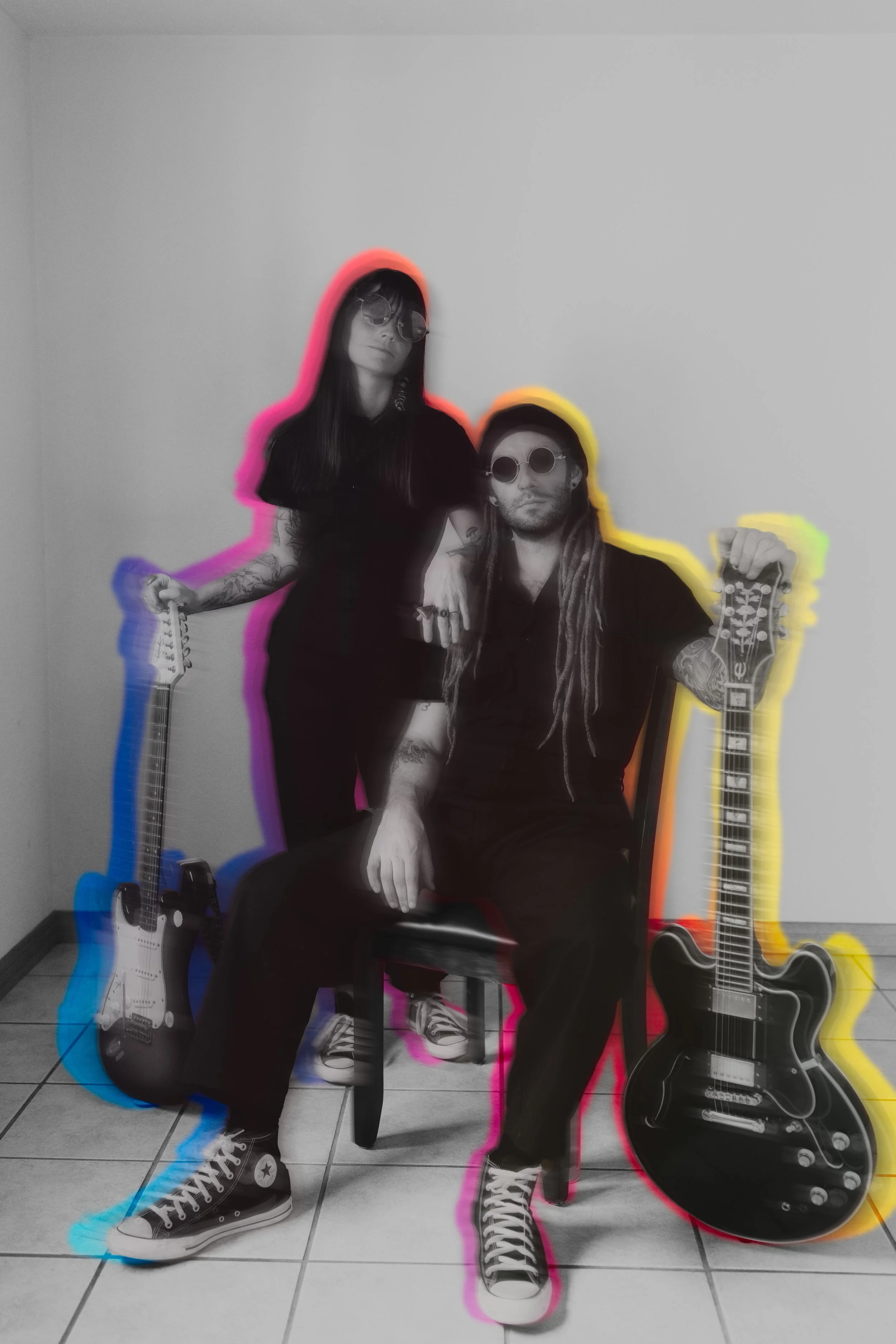 Black and white photo of a man and woman with guitars, sitting and standing against a plain wall, with colorful outlines around them in pink, blue, yellow, and orange.