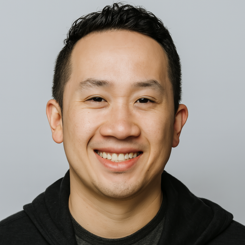 A smiling Asian man with short black hair, wearing a black jacket over a dark shirt, against a light gray background.
