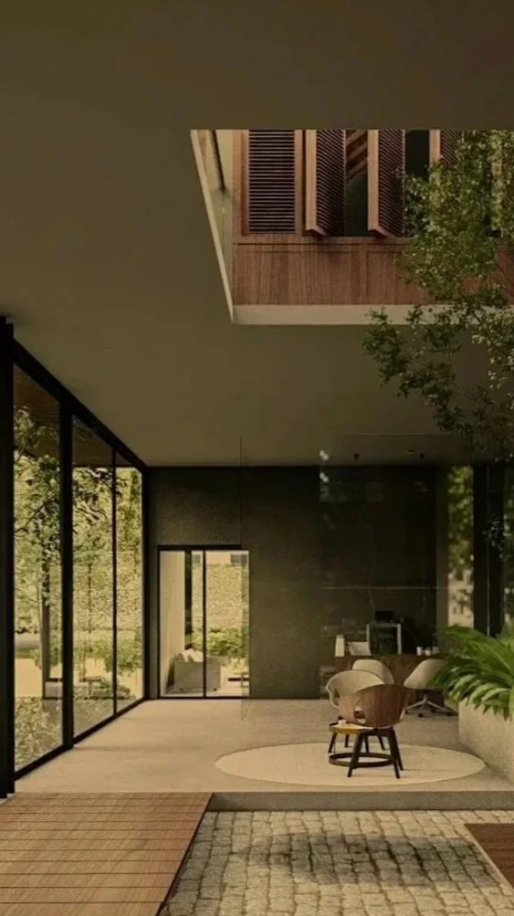 Modern indoor space with large floor-to-ceiling glass windows, a wooden floor section outside, and a seating area with chairs and a table near green plants.