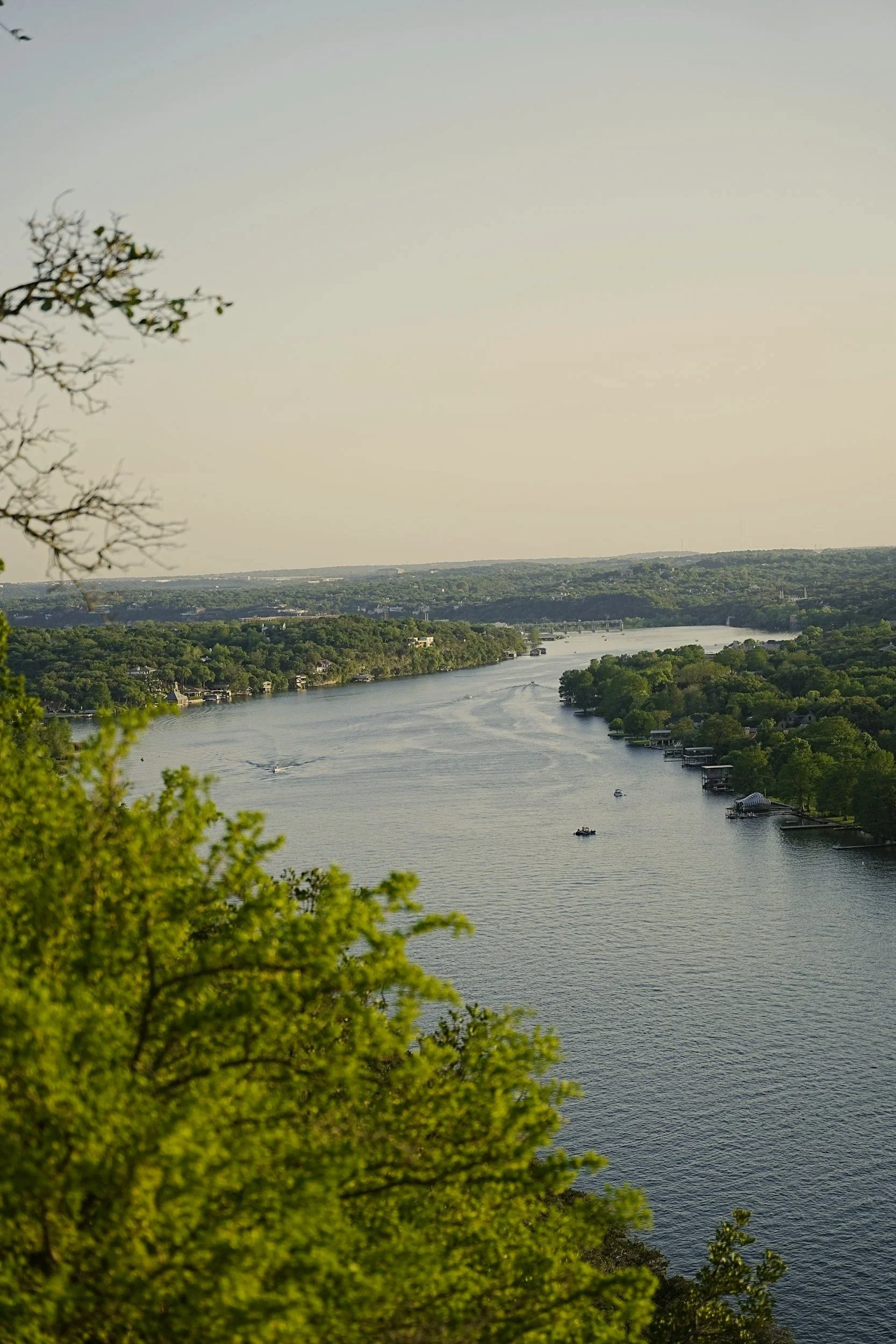 A scenic view of a river with boats and lush green trees along the shoreline, under a clear sky.