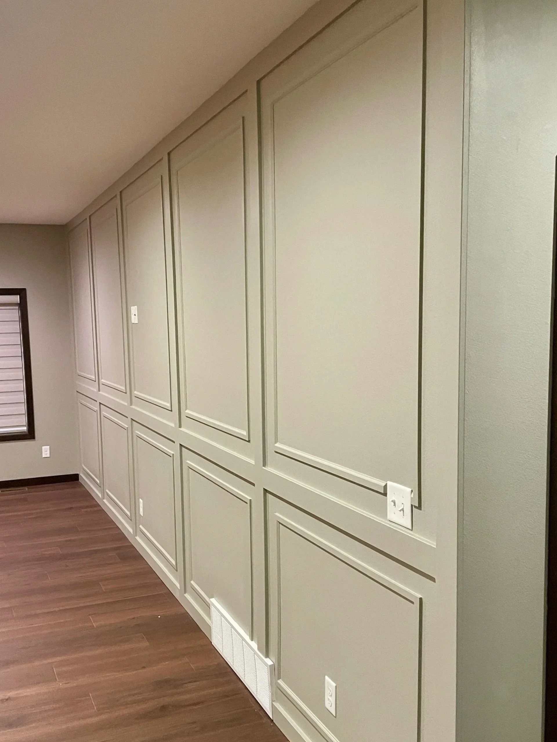 Living room with beige paneled wall, hardwood floor, and electrical outlets.