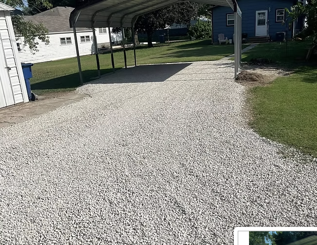 A gravel driveway leading to a metal carport in a residential backyard with grass and trees.