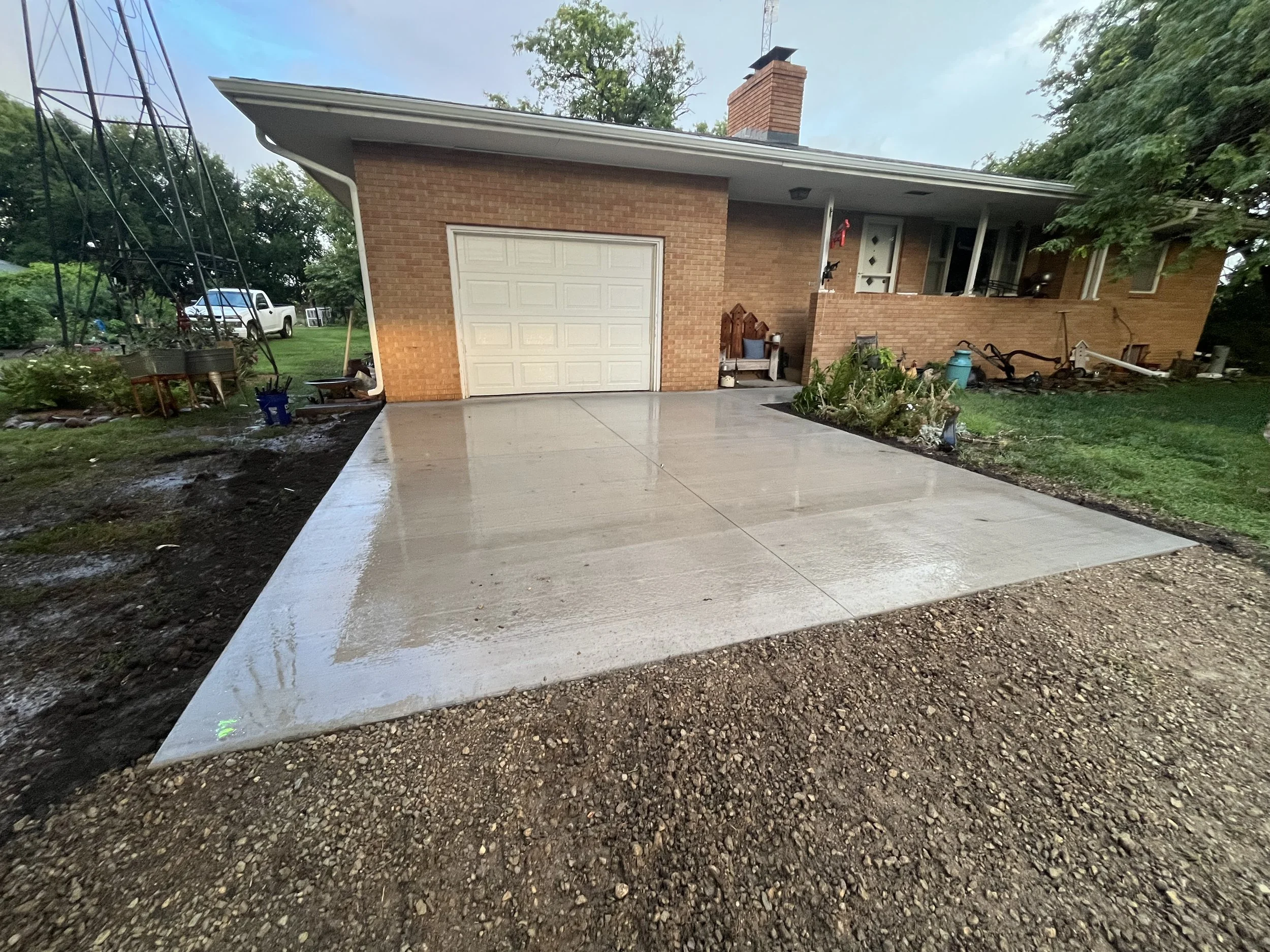 Newly poured concrete driveway in front of a brick house with a white garage door and a small porch.