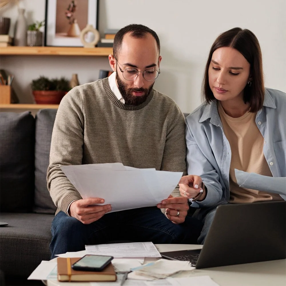 A man and woman sitting on a couch looking and reviewing documents together with a financial advisor in Redding, CA John Winn