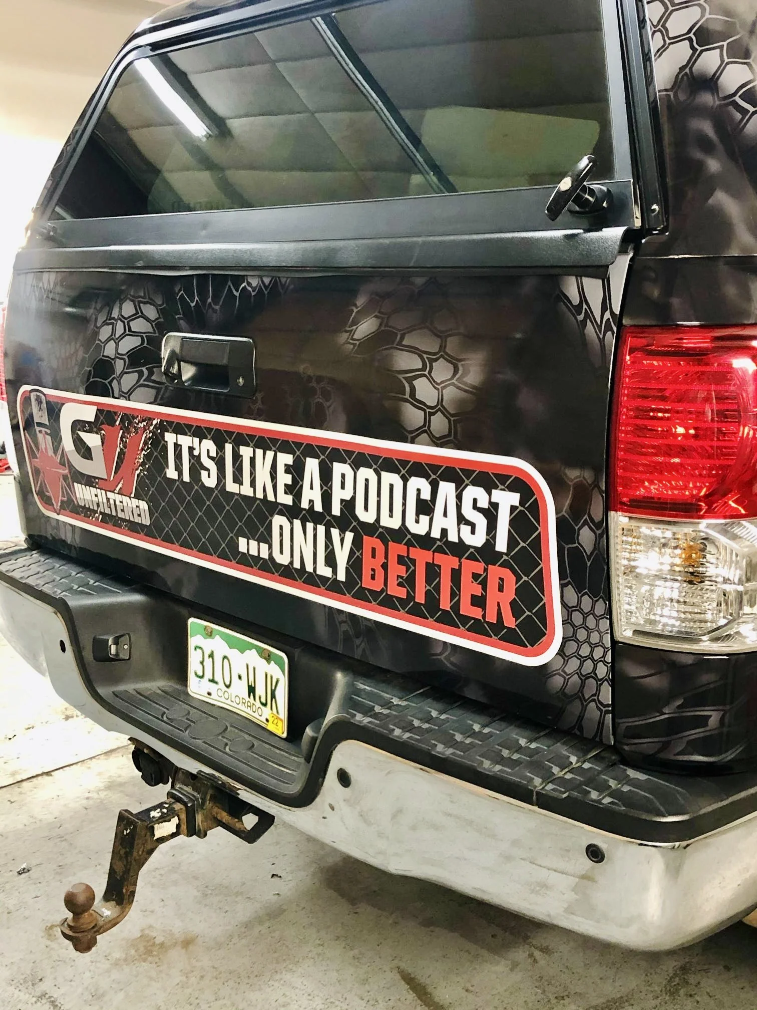 Back of a black pickup truck with a decal that reads "GJ Unfiltered, It's like a podcast ... only better" and a Colorado license plate.