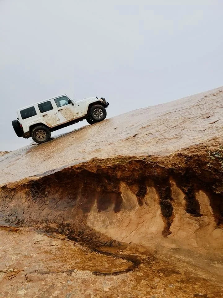 A white Jeep climbing a steep, rocky desert hill.