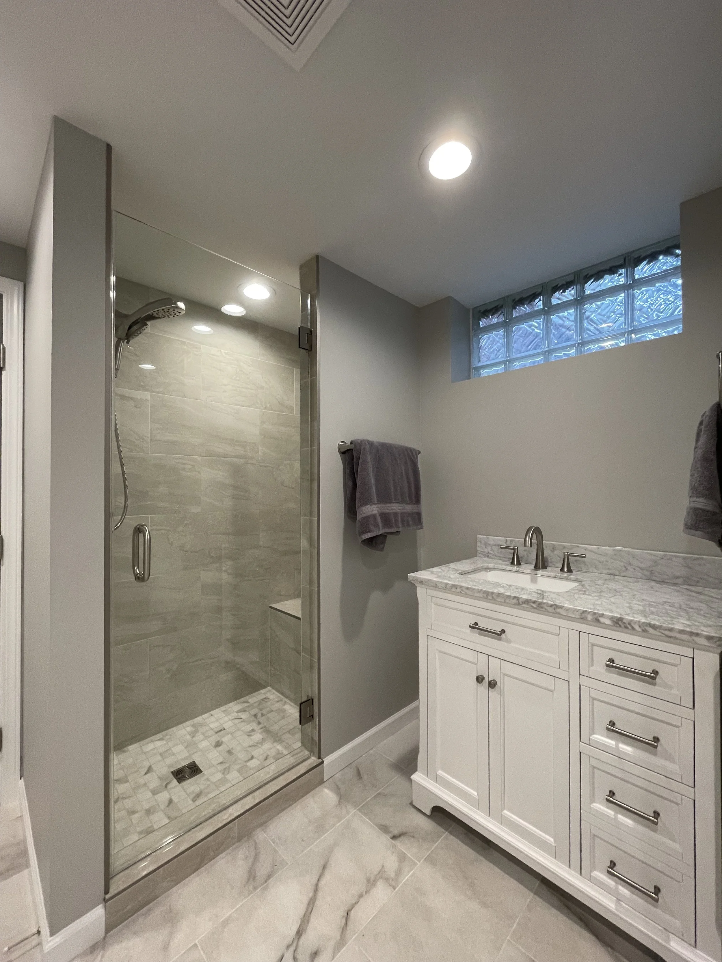 photo shows another view of the basement bathroom -- this one focuses on a close up of the tiled shower as well as the marble top vanity