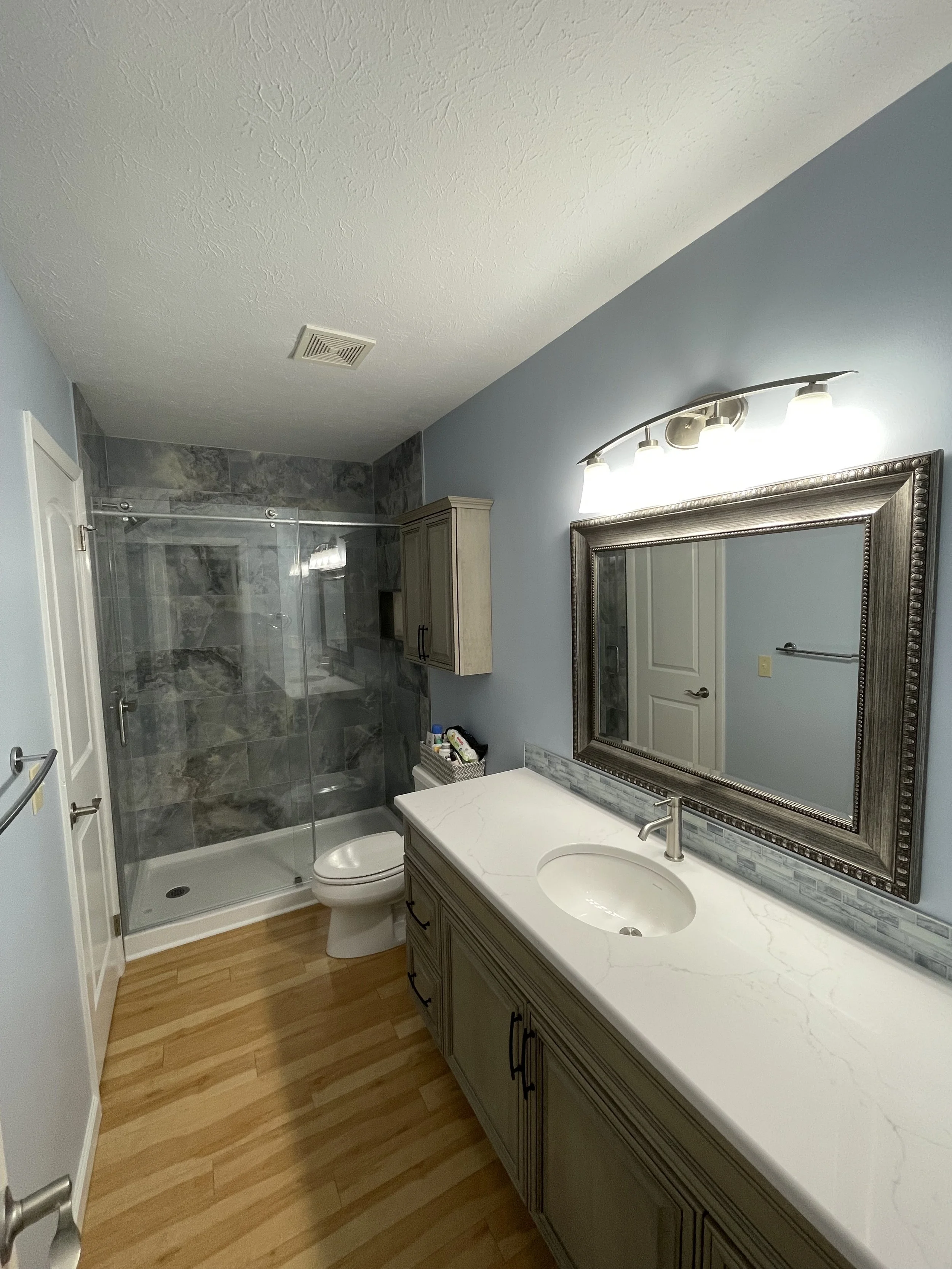 photo shows the countertop of a recent bathroom remodel -- a glass walk in shower is at the back of the photo