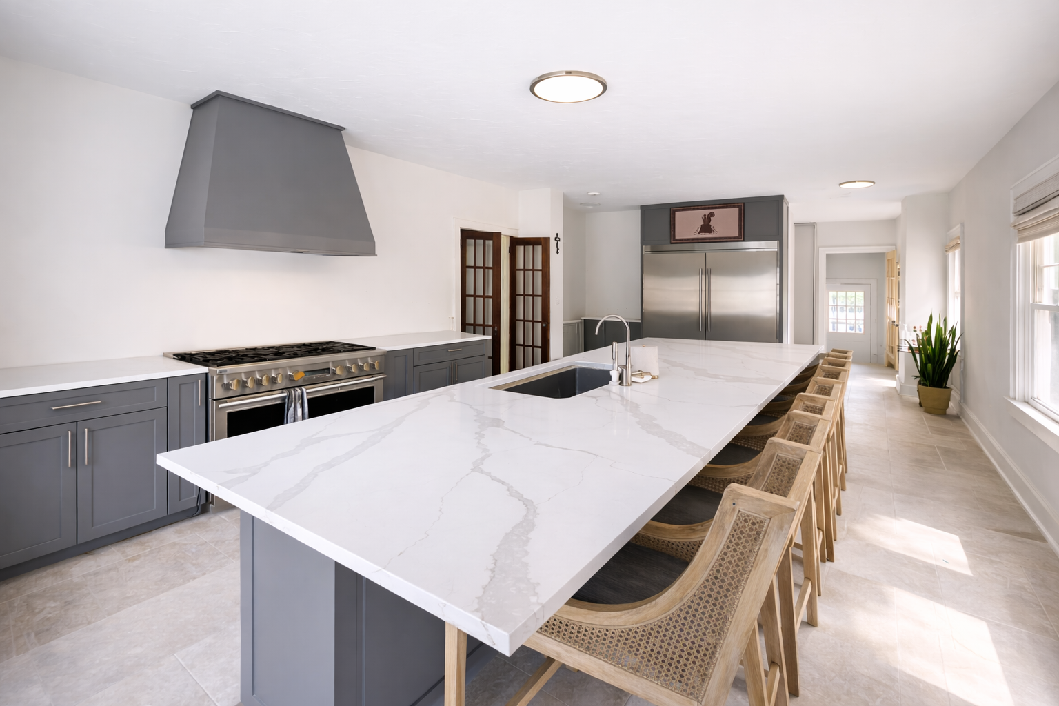 photo shows an open concept kitchen with a large marble countertop and accents of grey and white.