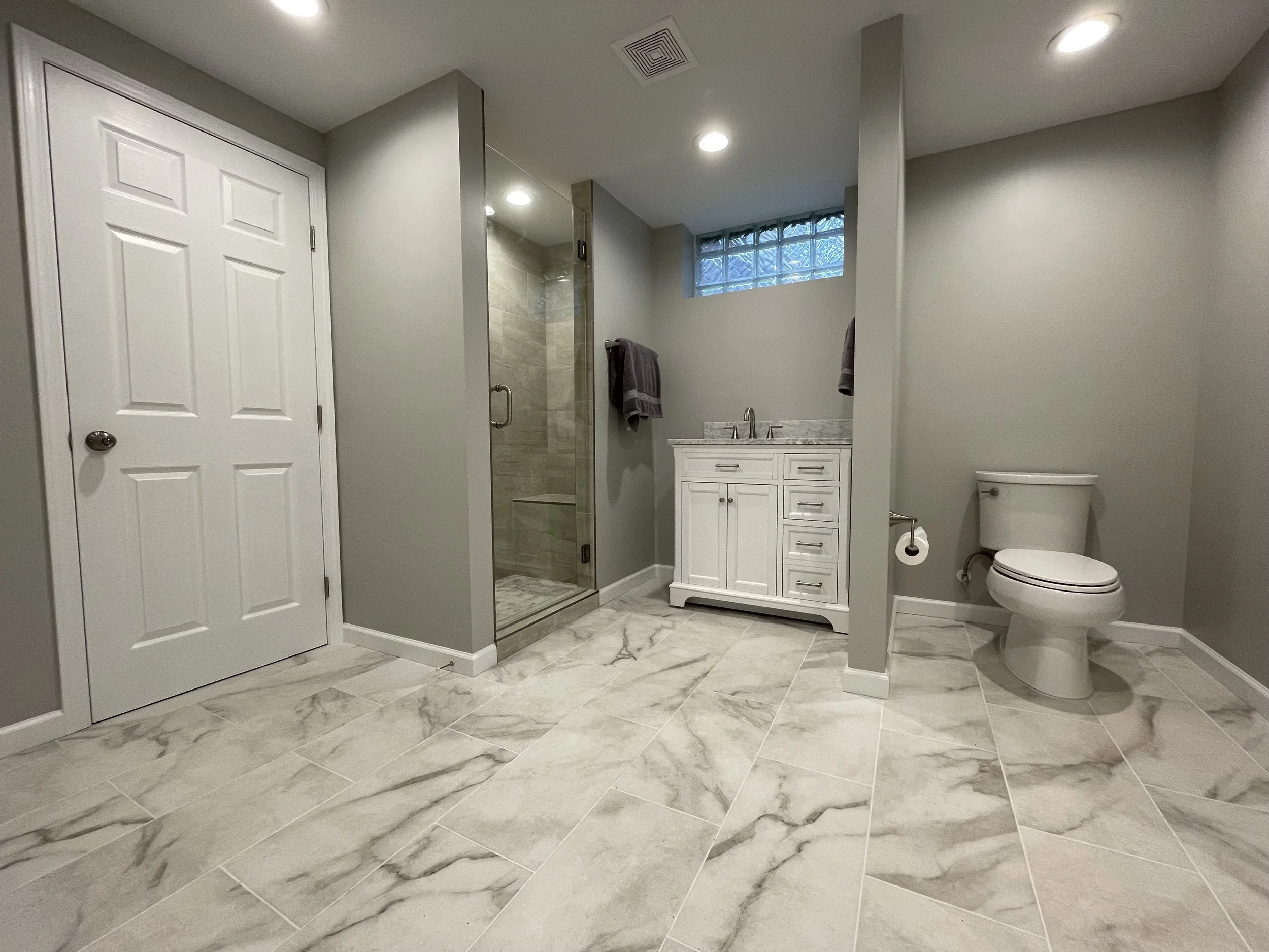 photo shows a basement bathroom with grey accents, it is bright and airy with a full shower