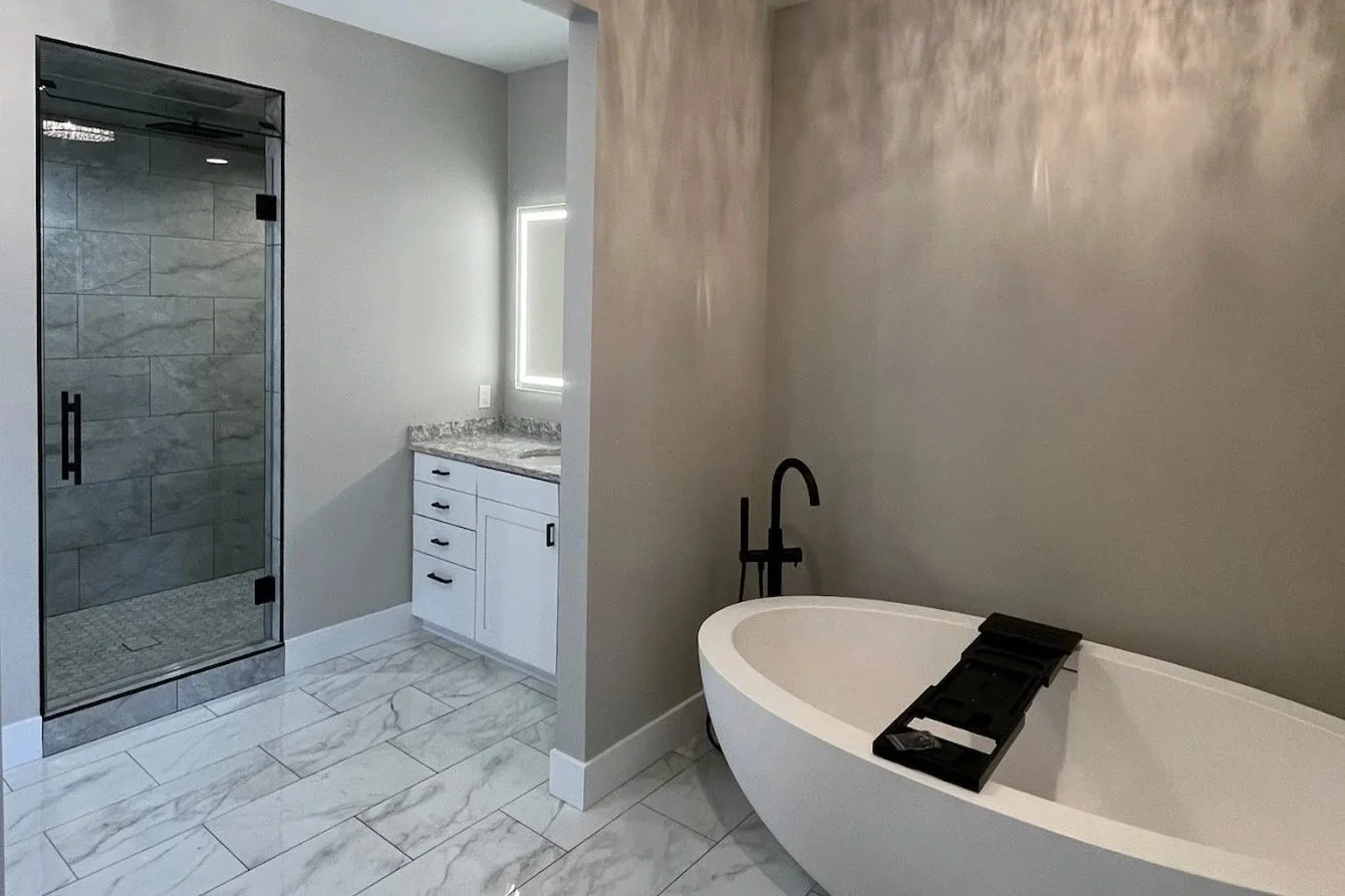 Modern bathroom with a with a stone-tiled shower, white vanity with black hardware, and a freestanding bathtub with a black faucet and tray.