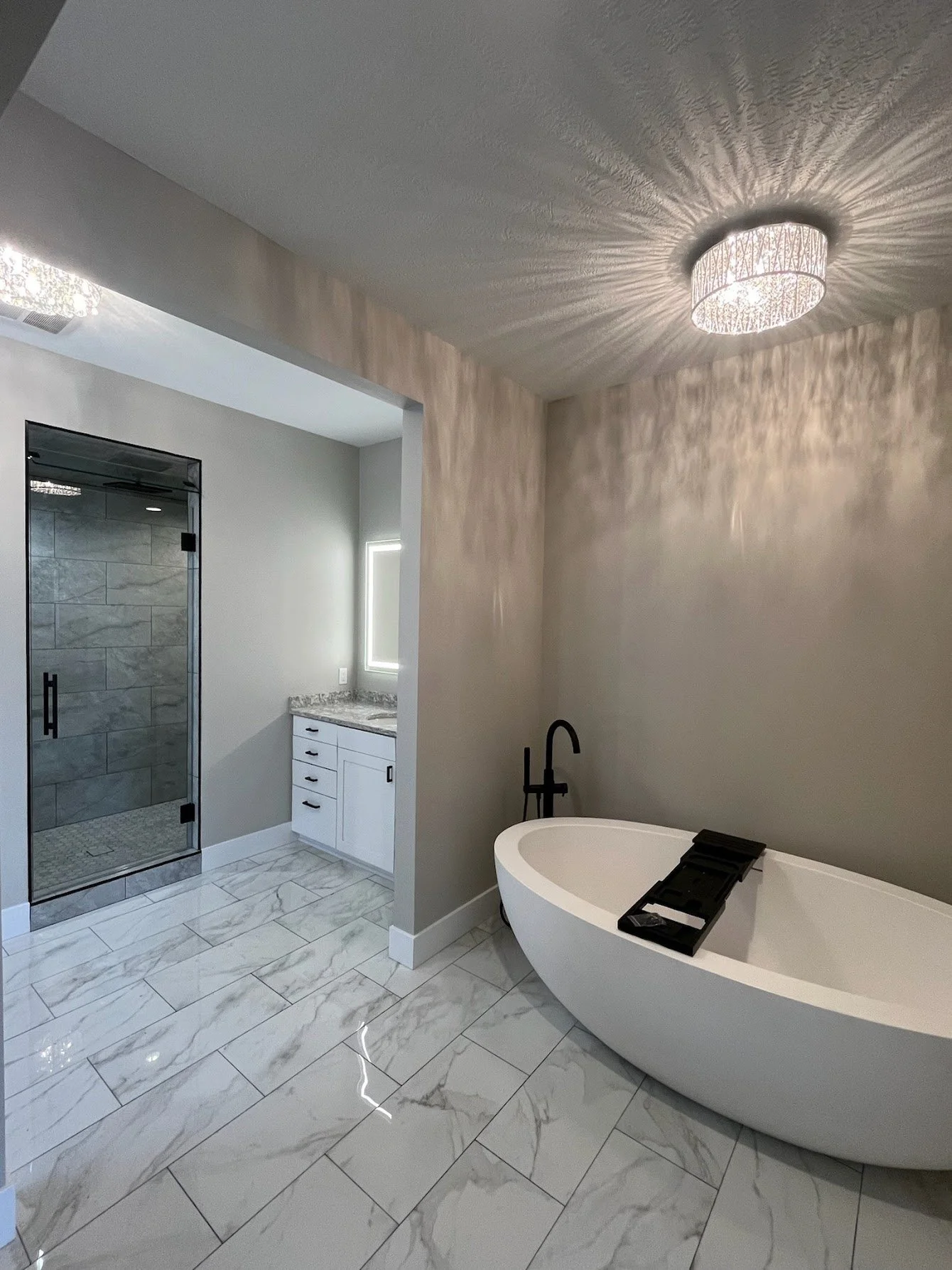 photo shows the full view of a modern bathroom remodel with grey large tiles, a soaker tub and glass walk in shower